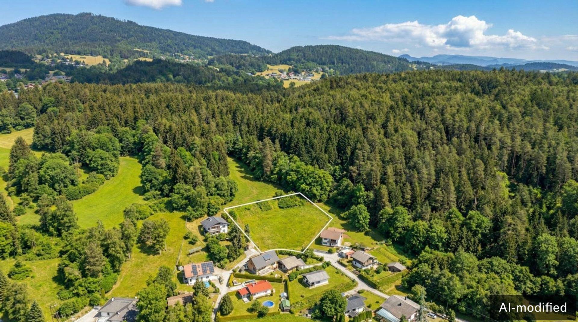 Luftaufnahme eines Wohngebiets mit einem großen, weiß umrandeten Grundstück, umgeben von Wald und Hügeln.