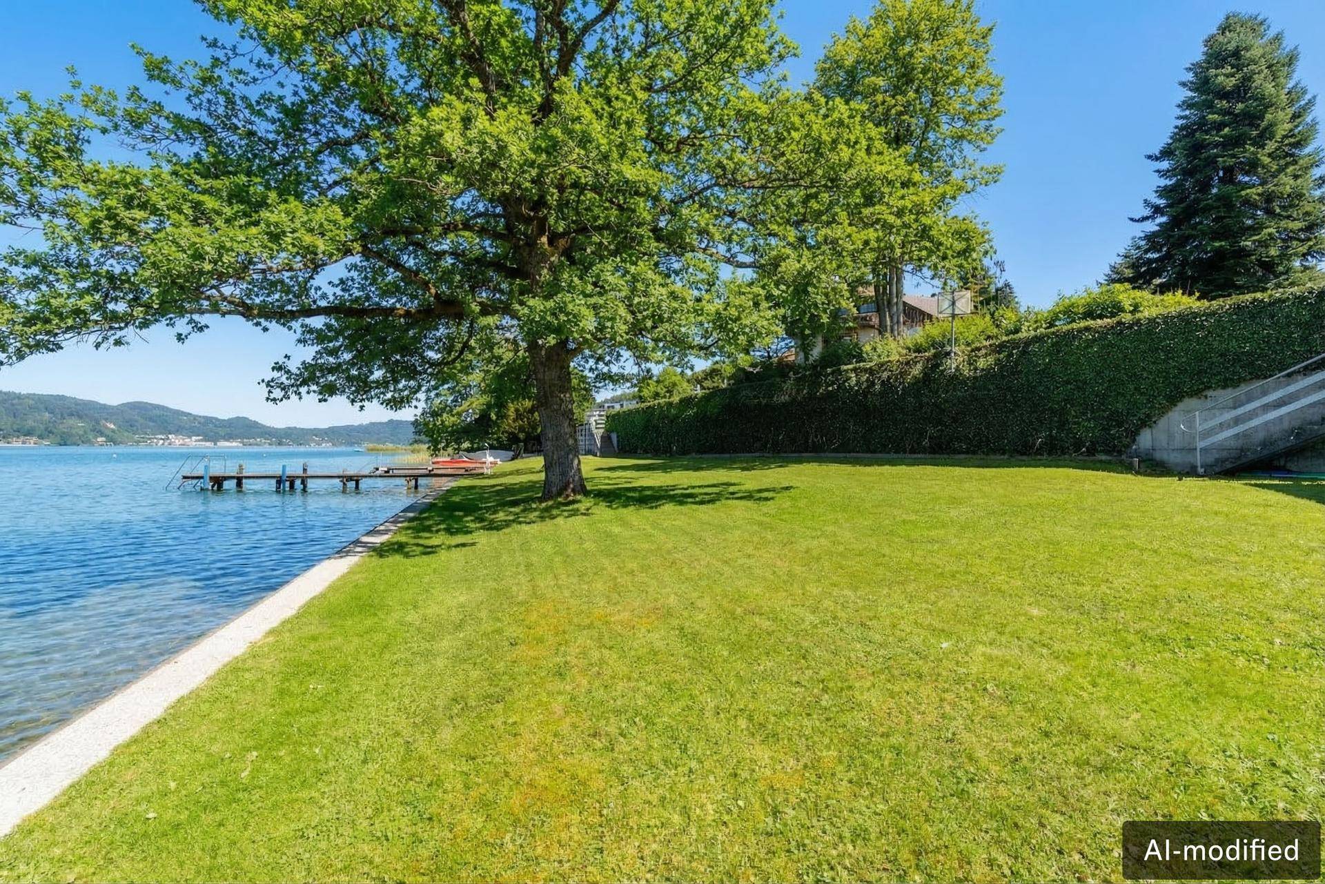 Gepflegte Rasenfläche am Seeufer mit altem Baum und Blick auf den See.