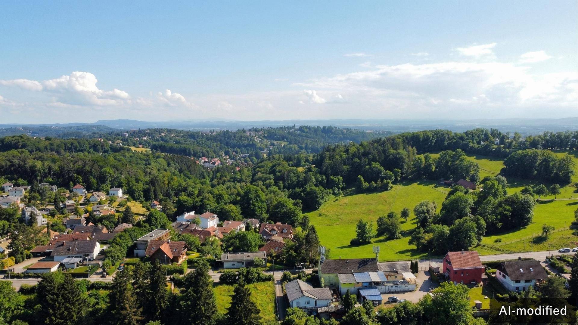 Panoramablick aus der Vogelperspektive auf eine ländliche Siedlung, umgeben von weiten Wäldern und Hügeln.