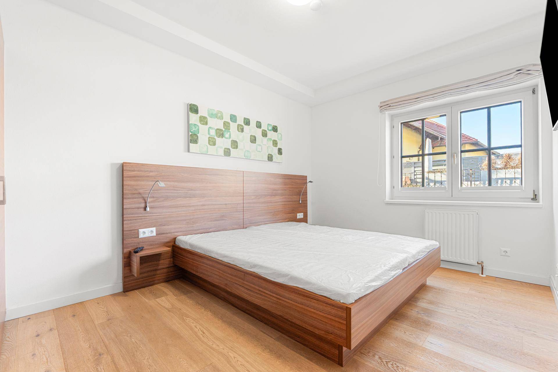 Helles Schlafzimmer mit Holzbett, Parkettboden und moderner Wanddekoration.