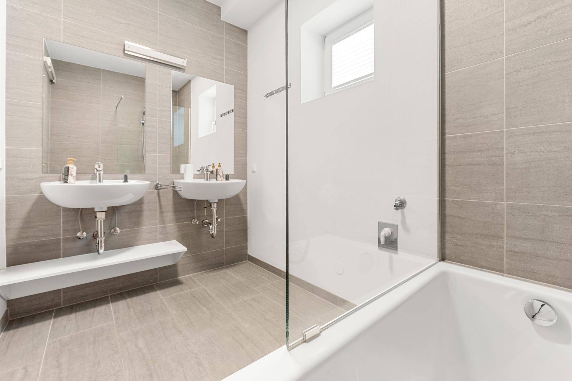 Modernes Badezimmer mit Doppelwaschbecken, Badewanne und großen Fliesen.