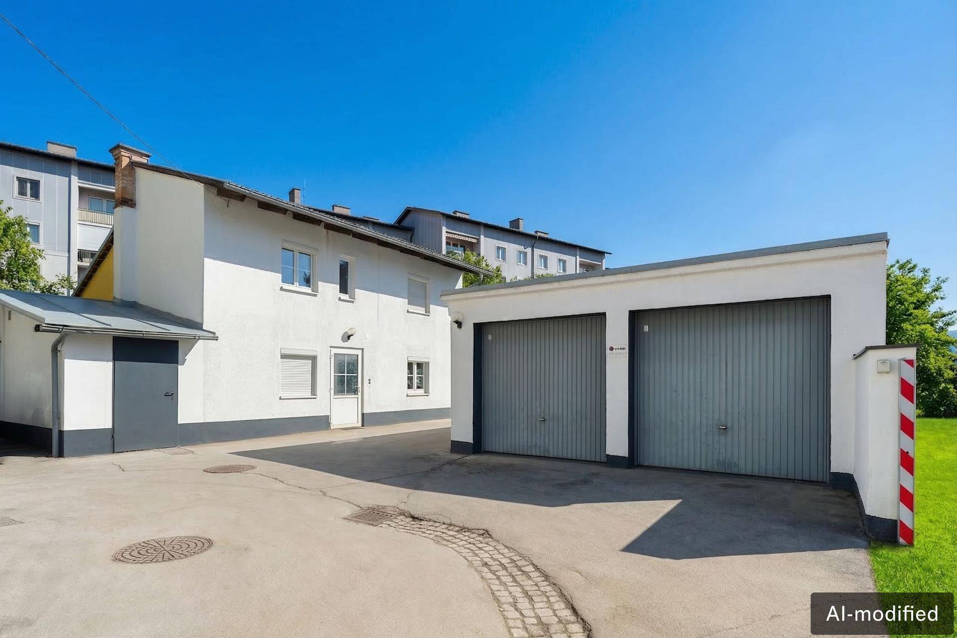Doppelgarage und Nebengebäude mit weißer Fassade und grauen Toren.