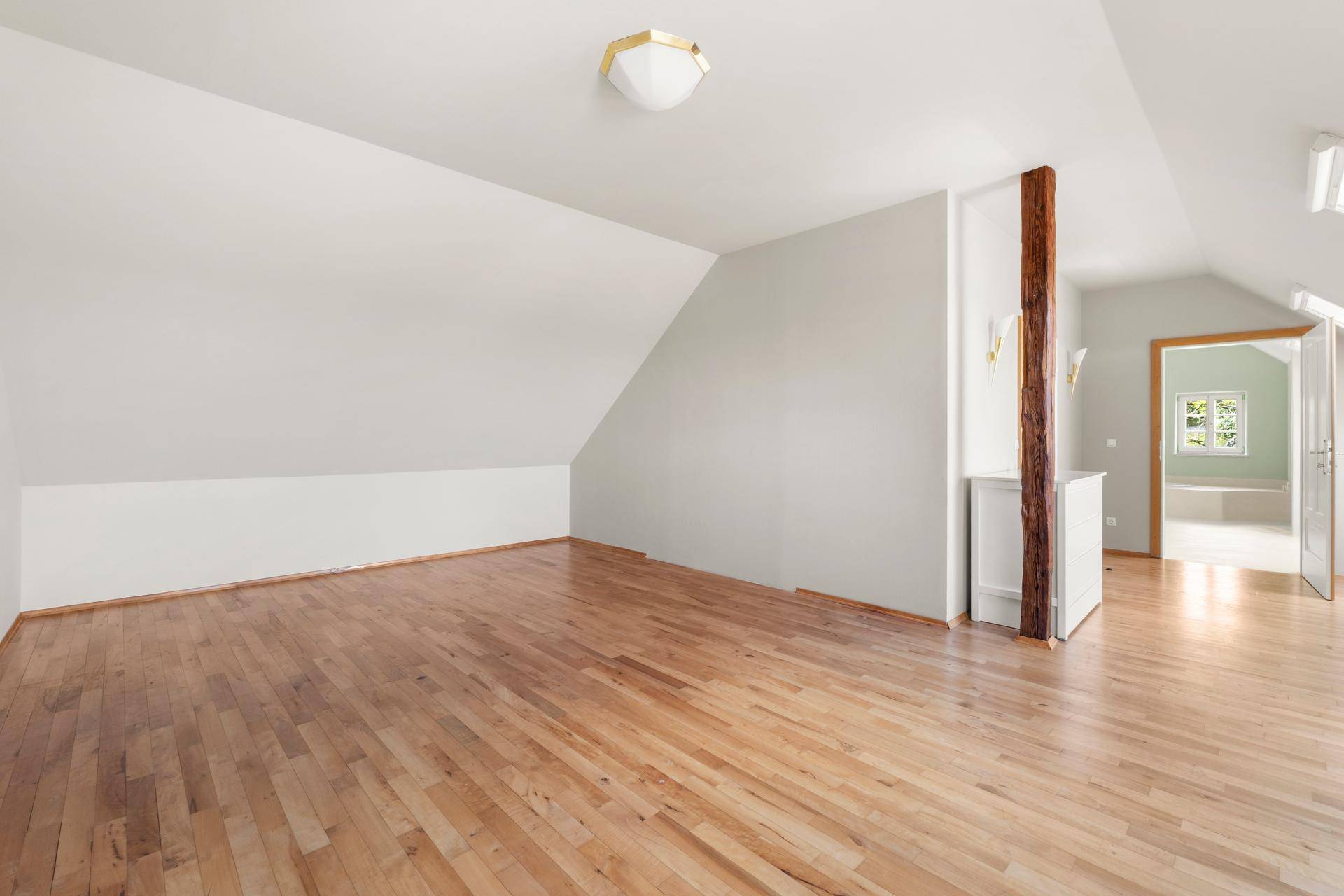 Helles Zimmer mit Holzboden, Dachschrägen und einem sichtbaren Holzbalken.