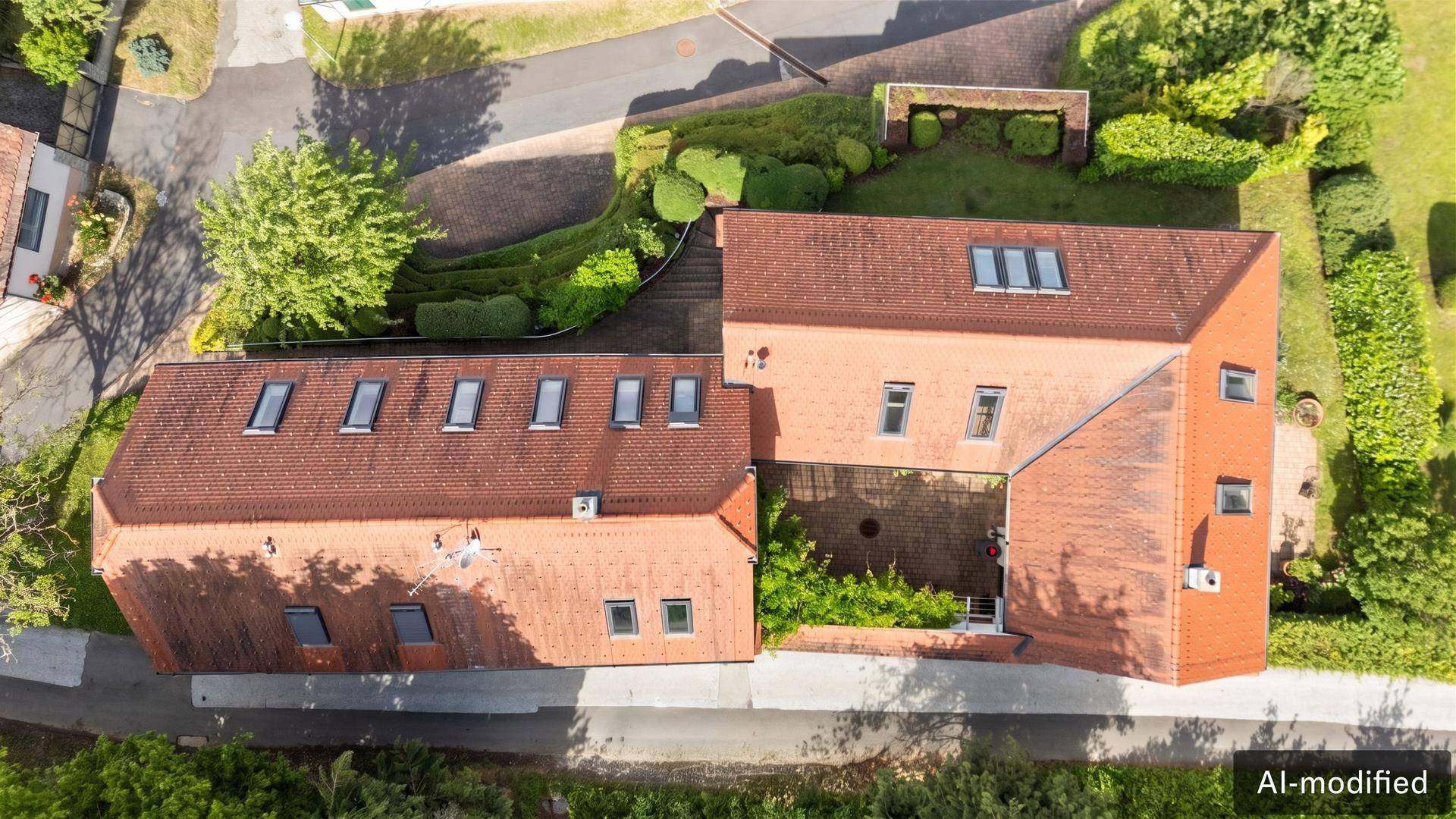 Luftaufnahme eines Gebäudekomplexes mit roten Ziegeldächern und vielen Dachfenstern.