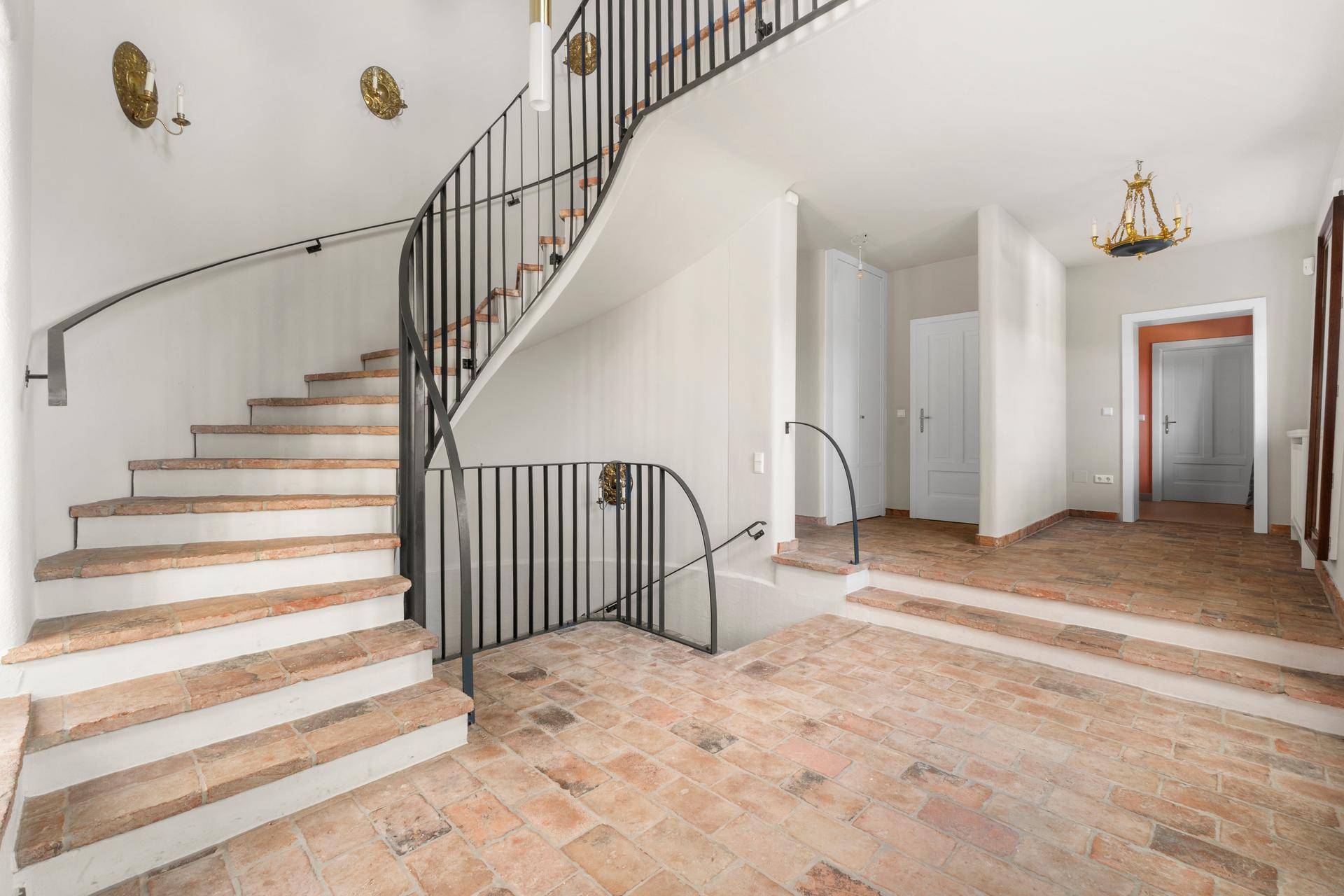 Elegante Eingangshalle mit geschwungener Treppe, Terrakotta-Bodenfliesen und dekorativen Wandleuchten.