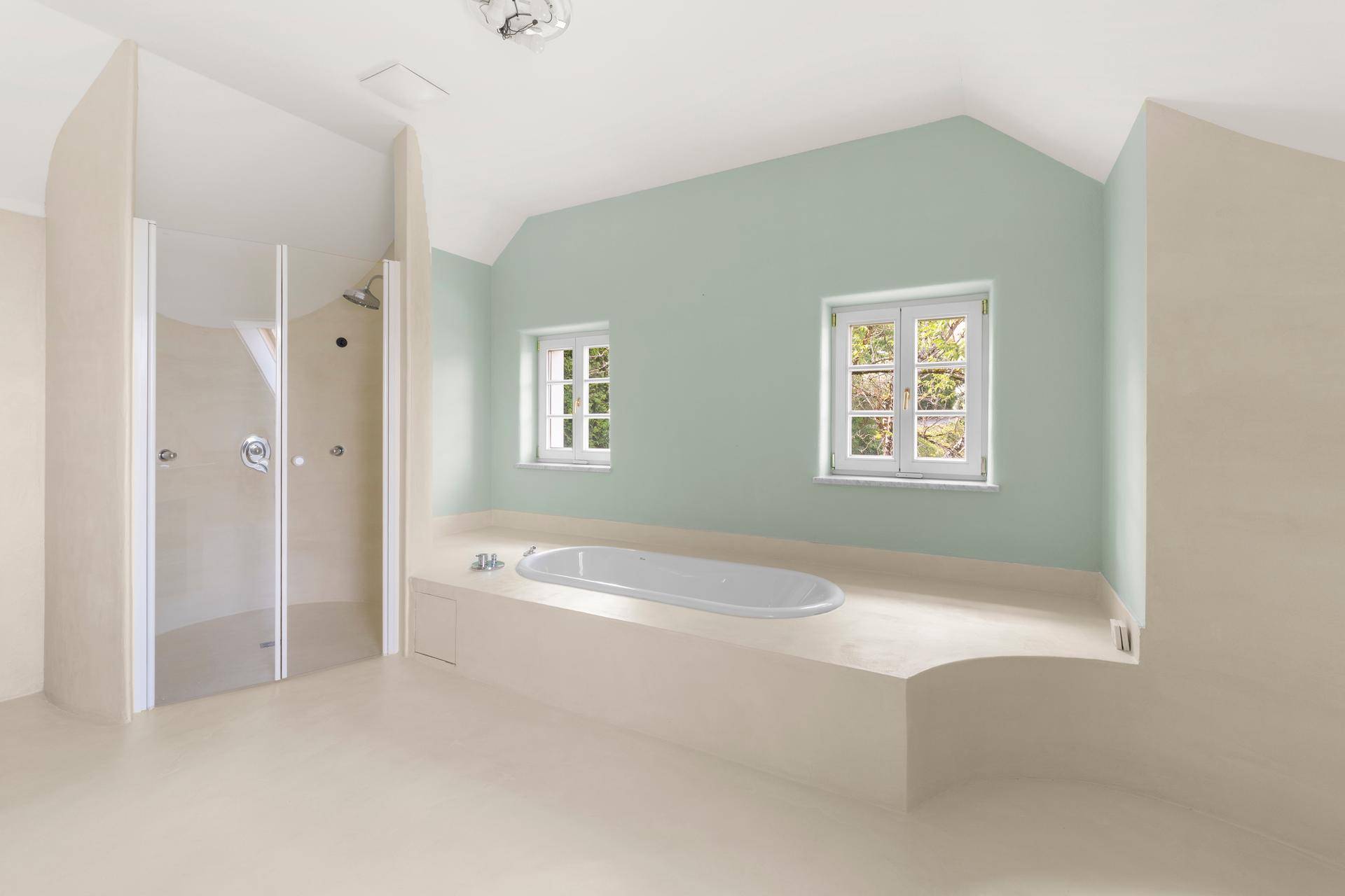 Helles Badezimmer mit integrierter Badewanne, separater Dusche und zwei Fenstern.