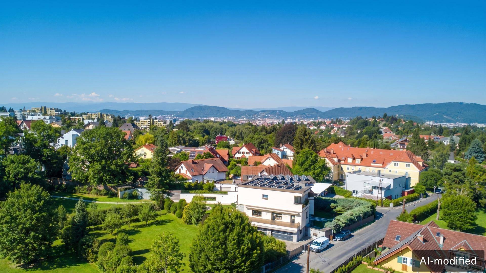 Eine weite Luftaufnahme einer Wohngegend mit Häusern, Bäumen und Bergen im Hintergrund.