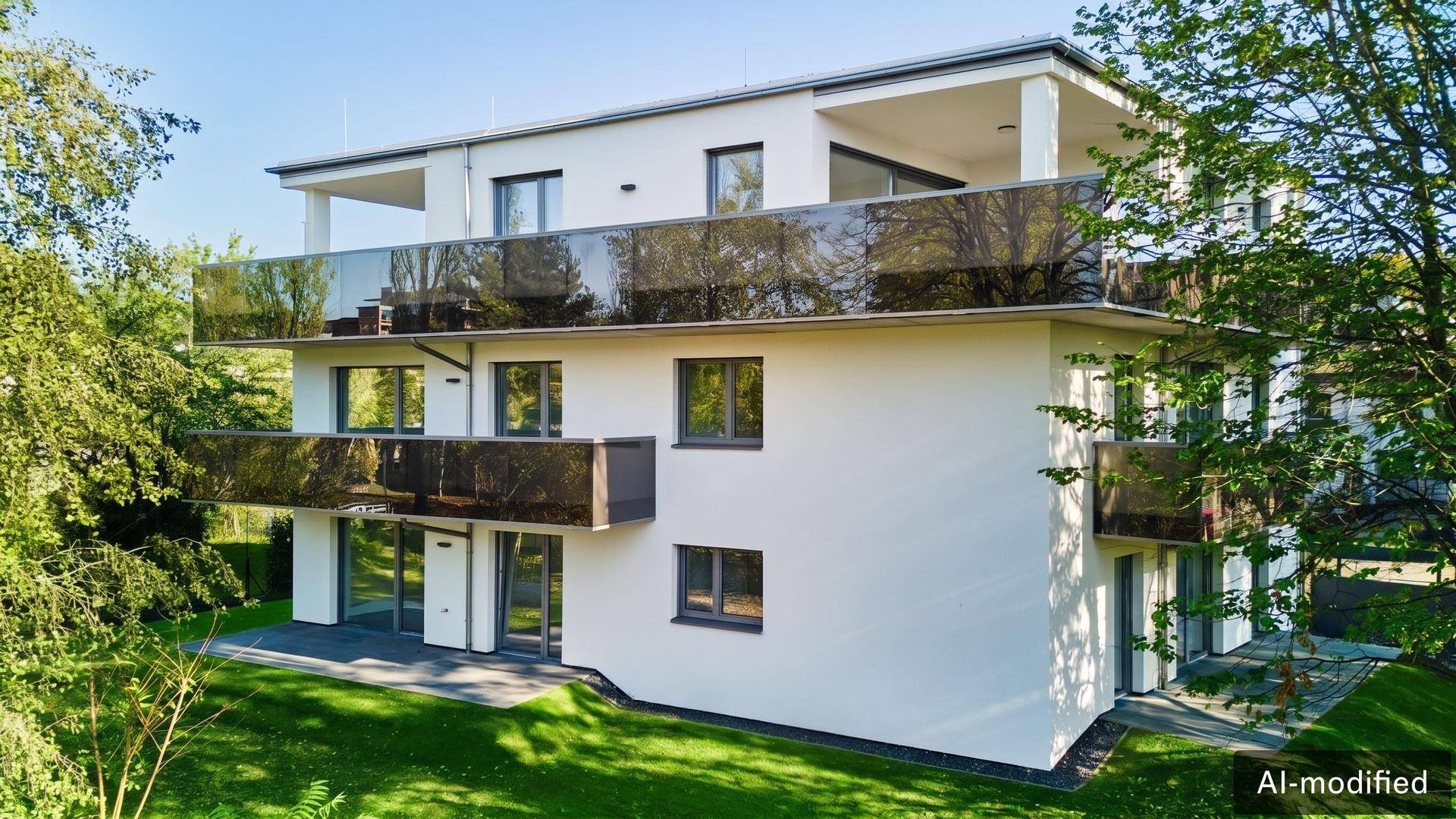 Modernes Wohngebäude mit weißer Fassade, großen Fenstern und Glasbalkonen umgeben von Bäumen.