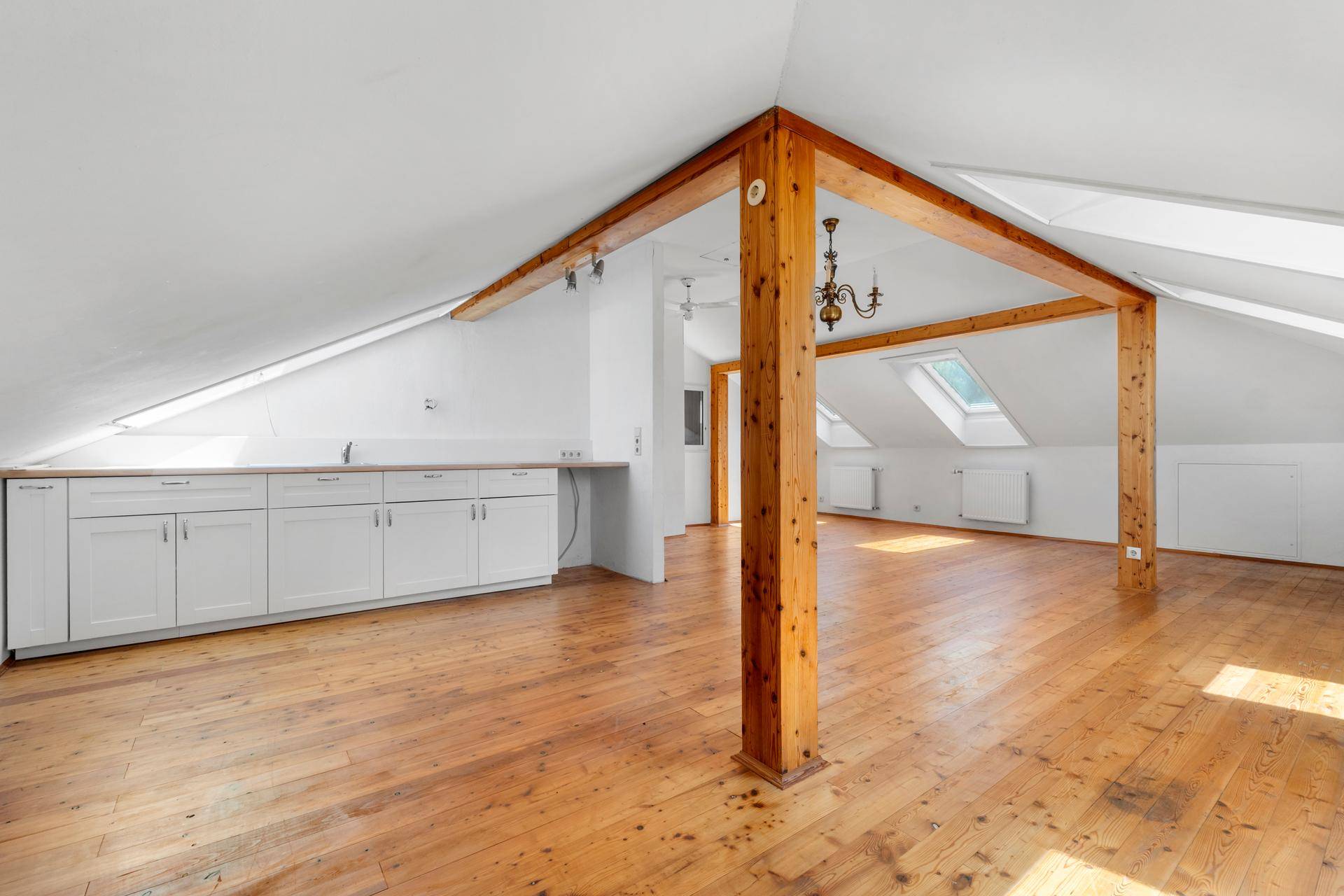 Heller Dachbodenraum mit Einbauschränken, Holzbalken und Dachfenstern, ideal für ein Studio.