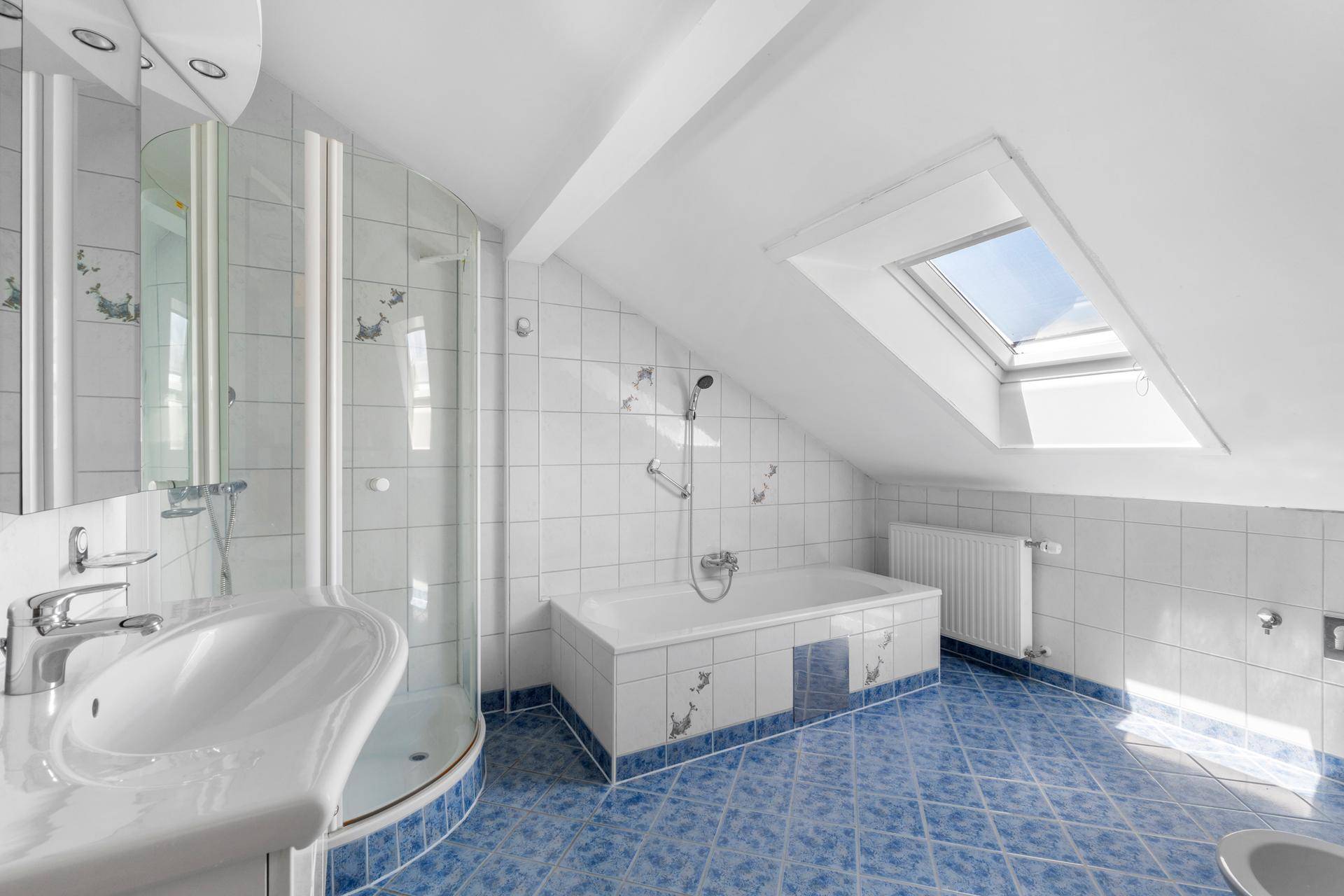 Badezimmer mit Badewanne, Duschkabine, Dachfenster und blauen Fliesen im Dachgeschoss.