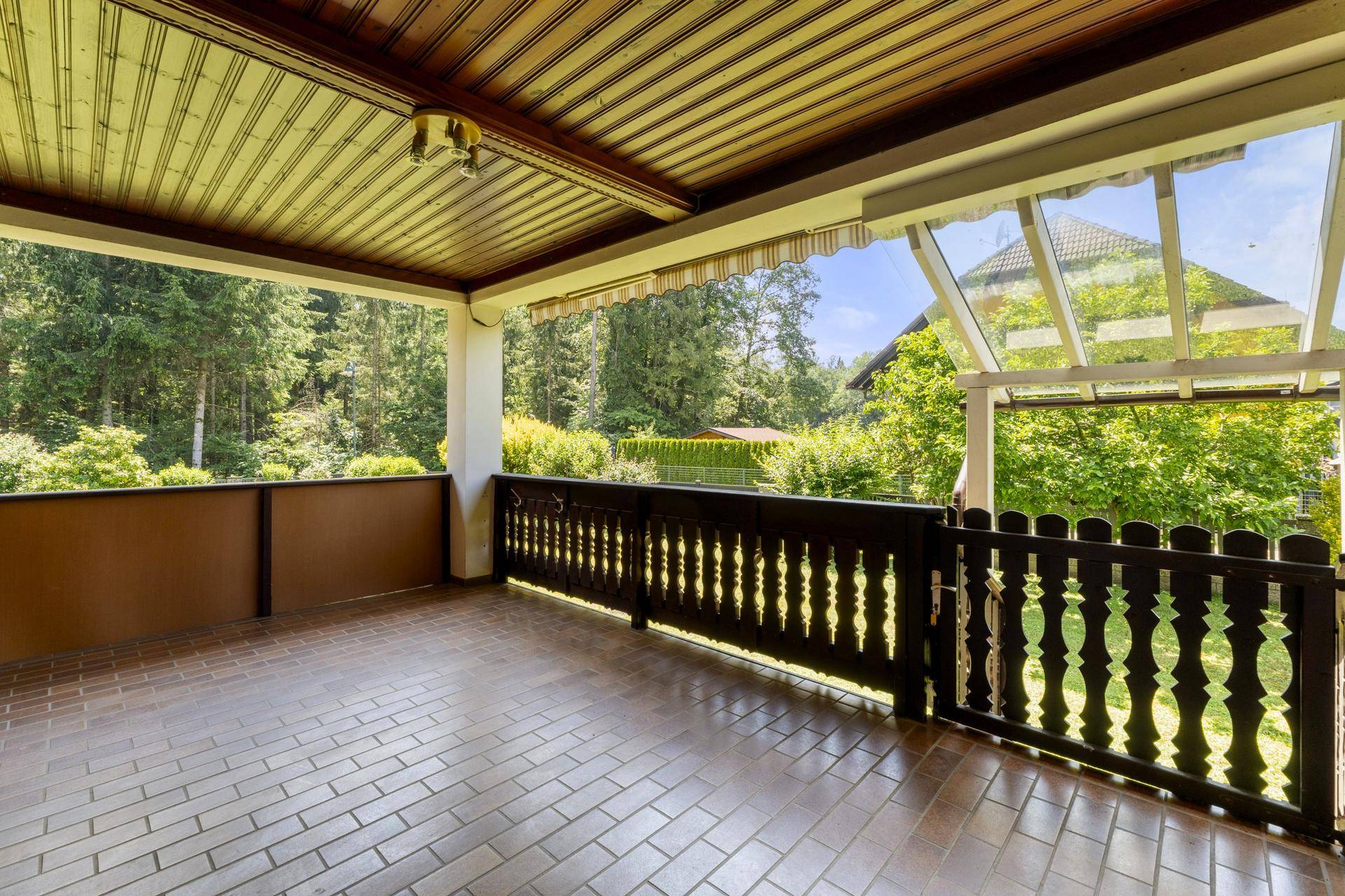 Großer überdachter Balkon mit Holzboden und Geländer, bietet einen schönen Blick ins Grüne.