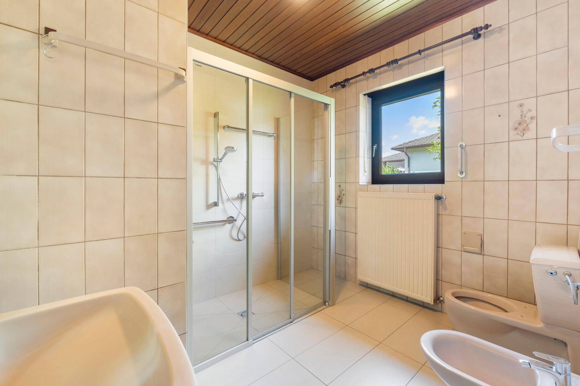Funktionales Badezimmer mit Duschkabine, Bidet, Fenster und praktischen Haltegriffen.