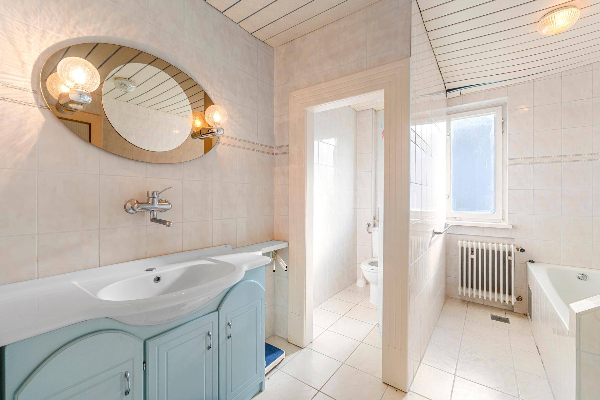 Helles Badezimmer mit weiß gefliesten Wänden, Einzelwaschbecken und Badewanne.