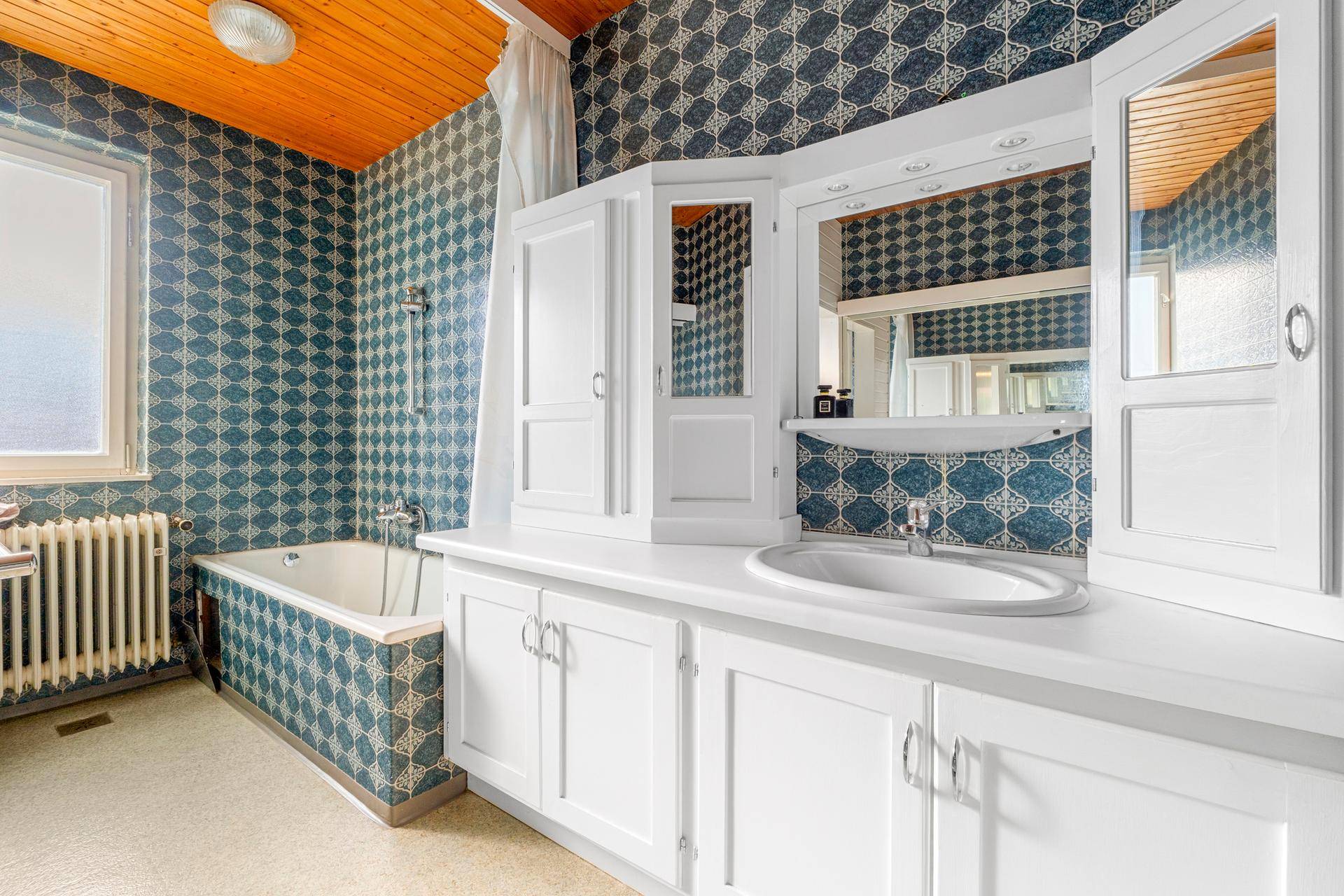Badezimmer mit auffälligen blauen Fliesen, Badewanne und großem Spiegelschrank.