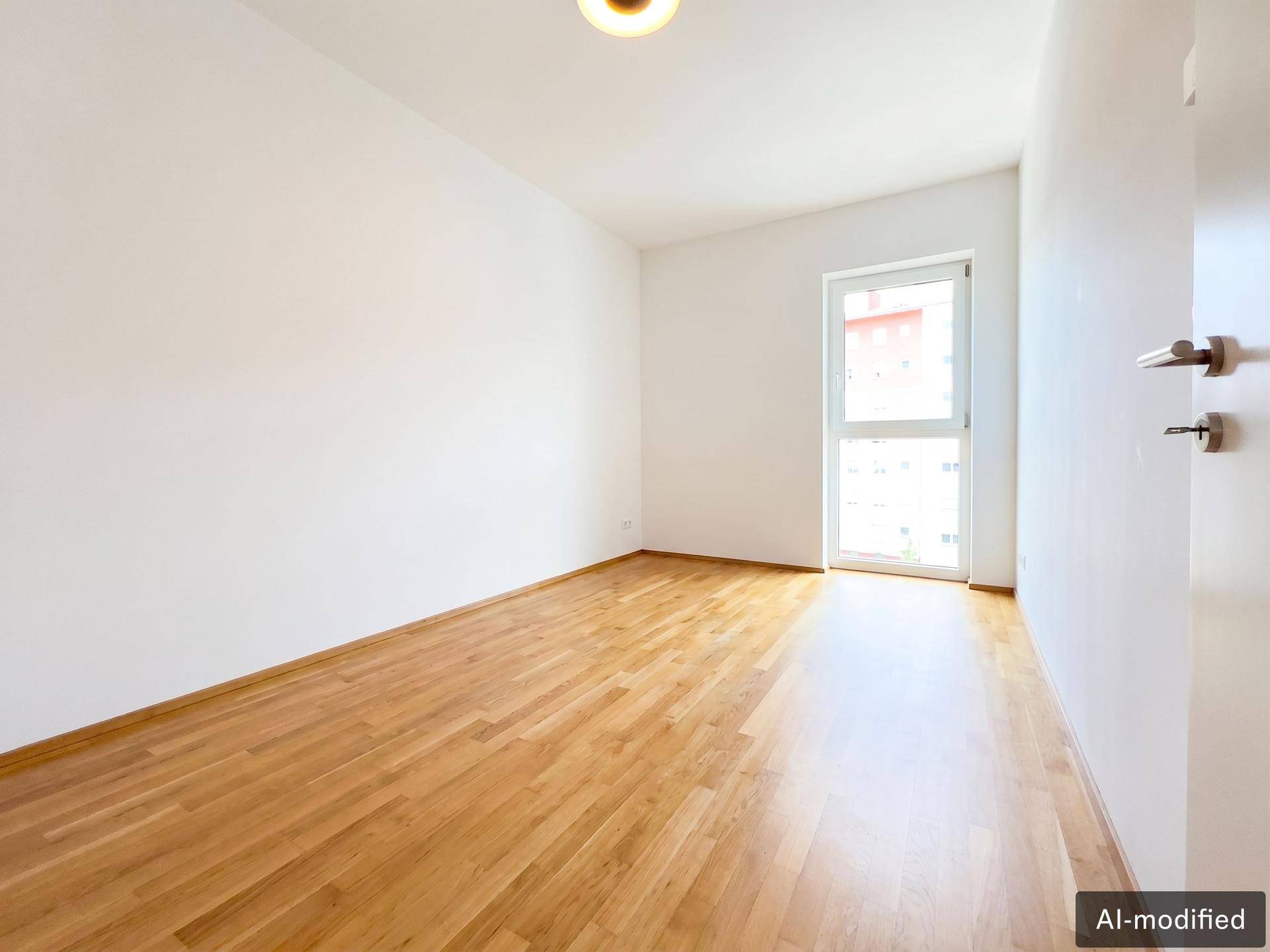 Leeres Schlafzimmer mit hellem Holzboden und einem großen Fenster, das viel Tageslicht hereinlässt.