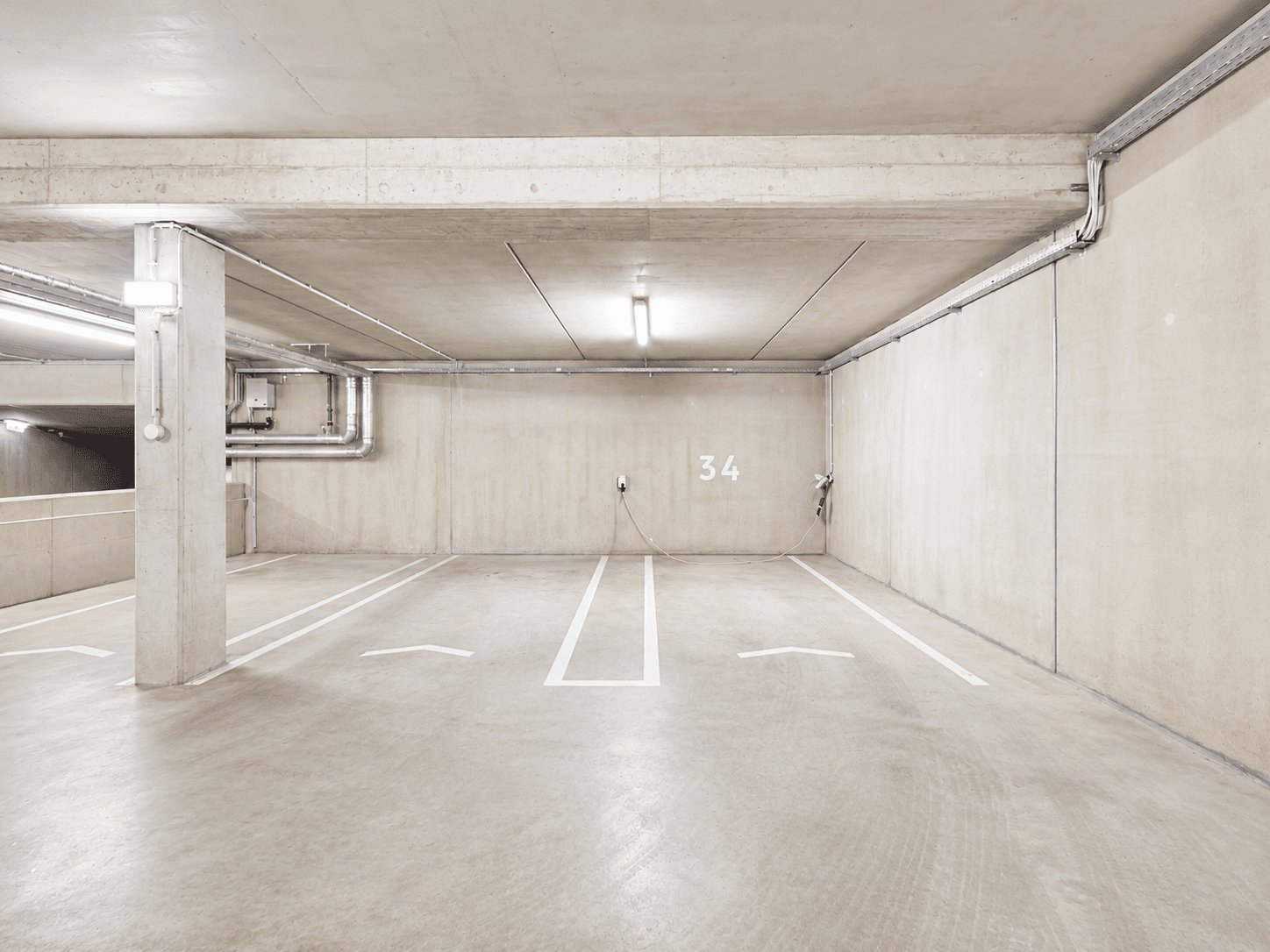 Tiefgarage mit Betonwänden, markierten Stellplätzen und Ladestationen für Elektrofahrzeuge.