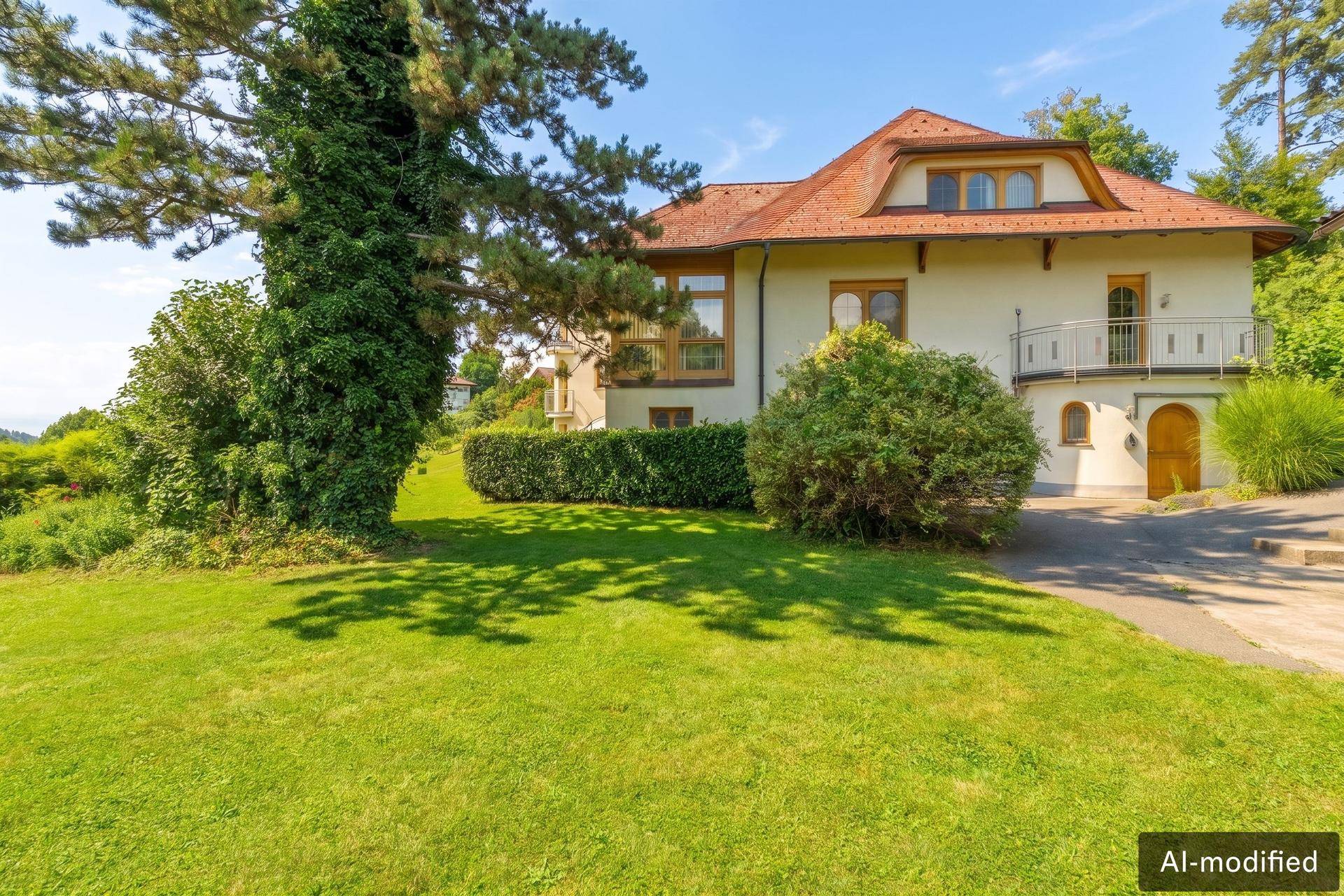 Seitenansicht der Villa mit gepflegtem Rasen, hohen Bäumen und einem kleinen Balkon.