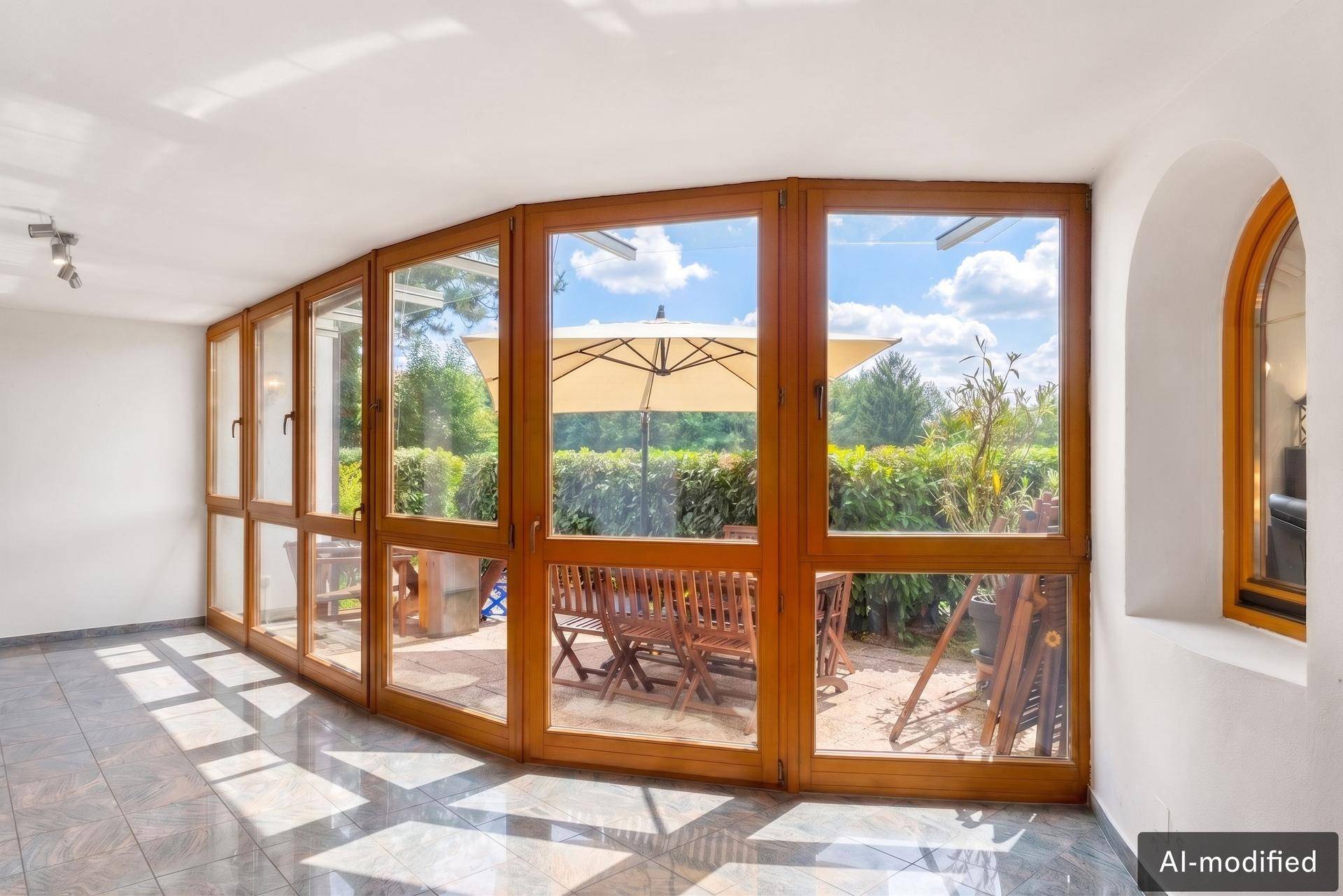 Geräumiger Wintergarten mit großen Fenstern, die den Blick auf die Terrasse freigeben.