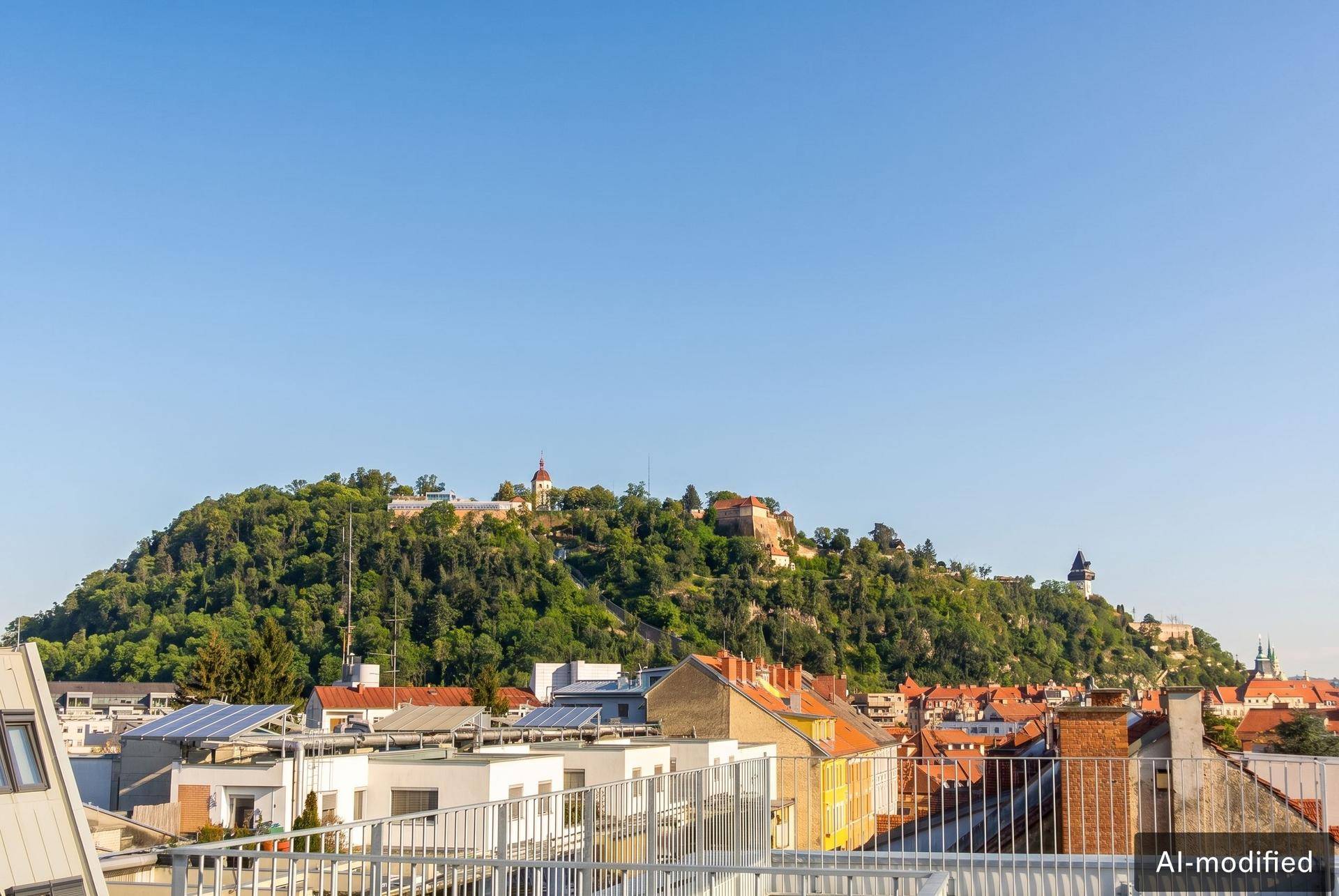 Panoramablick über die Stadt Graz mit dem bewaldeten Schlossberg und dem Uhrturm im Hintergrund.