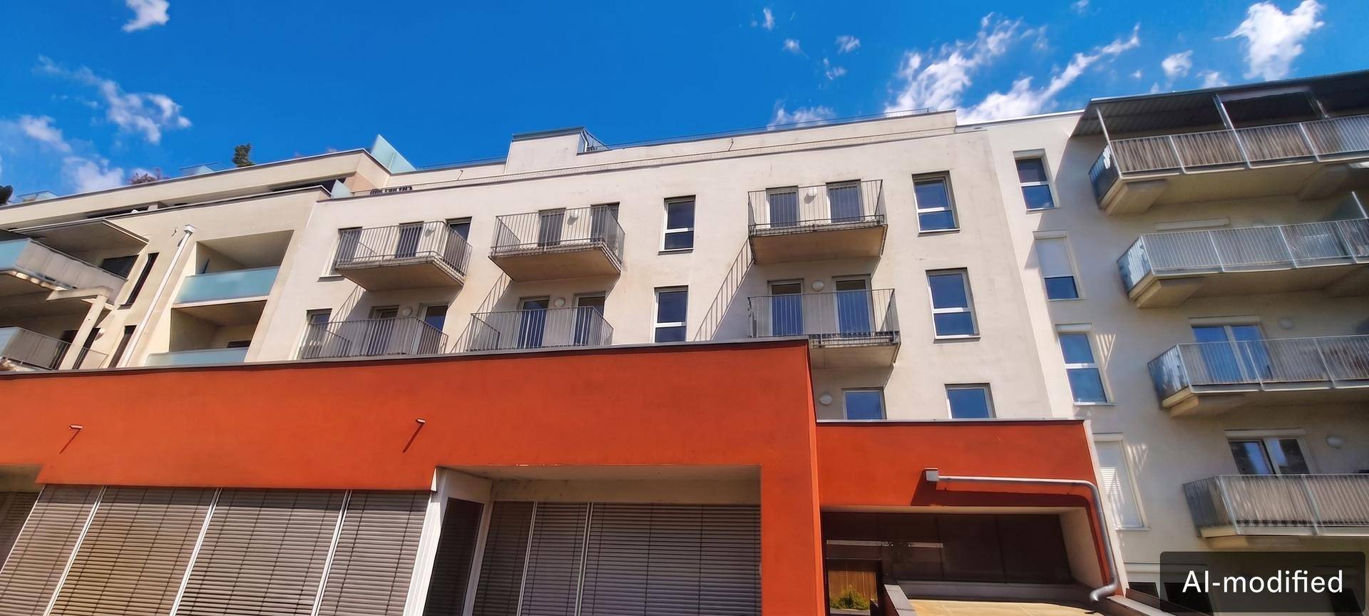 Moderne Wohnfassade mit weißen Wänden, roten Akzenten und mehreren Balkonen unter blauem Himmel.