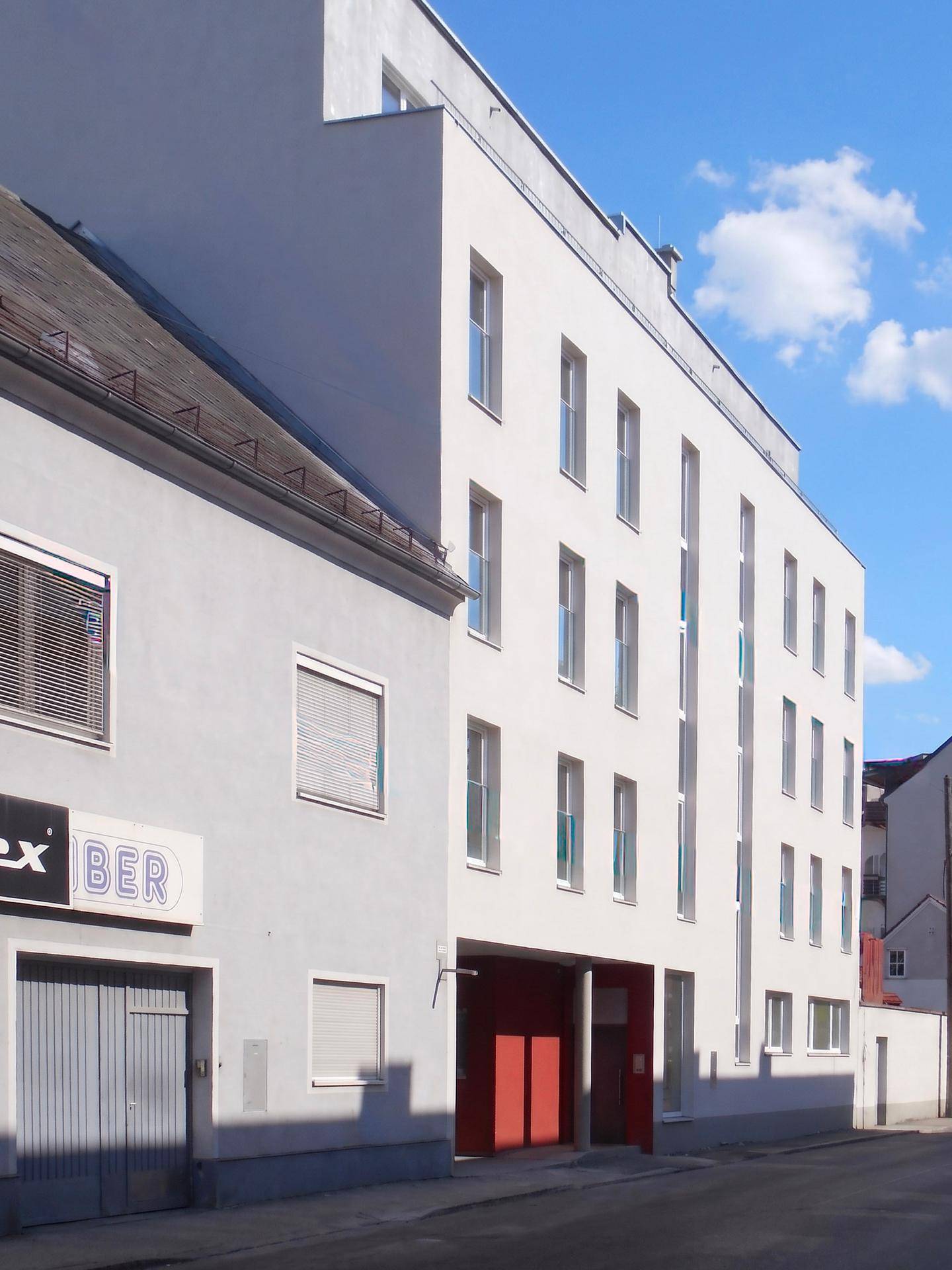 Seitenansicht eines modernen weißen Gebäudes neben einem älteren Bau mit Werbeschildern.