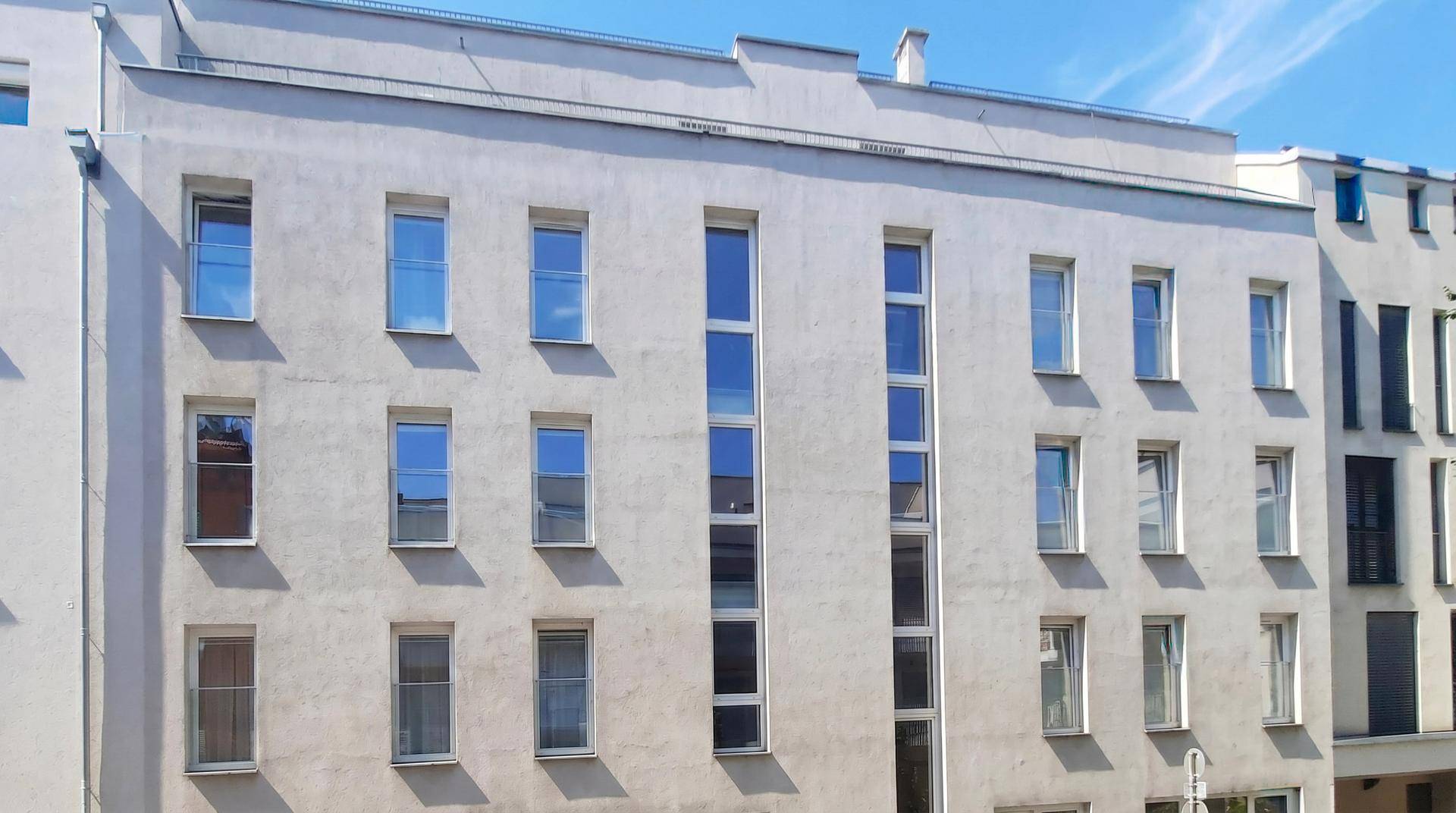 Klare Fassade eines modernen Wohngebäudes mit vielen Fenstern und schlichtem Design.