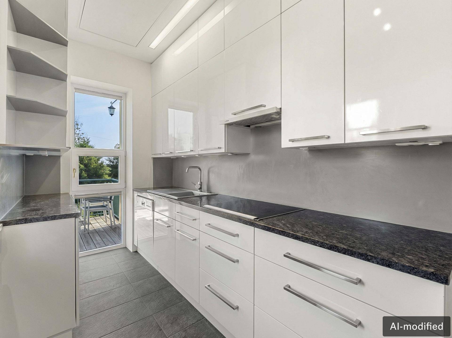 Moderne Küche mit weißen Hochglanzfronten, dunkler Arbeitsplatte und Zugang zu einem kleinen Balkon.