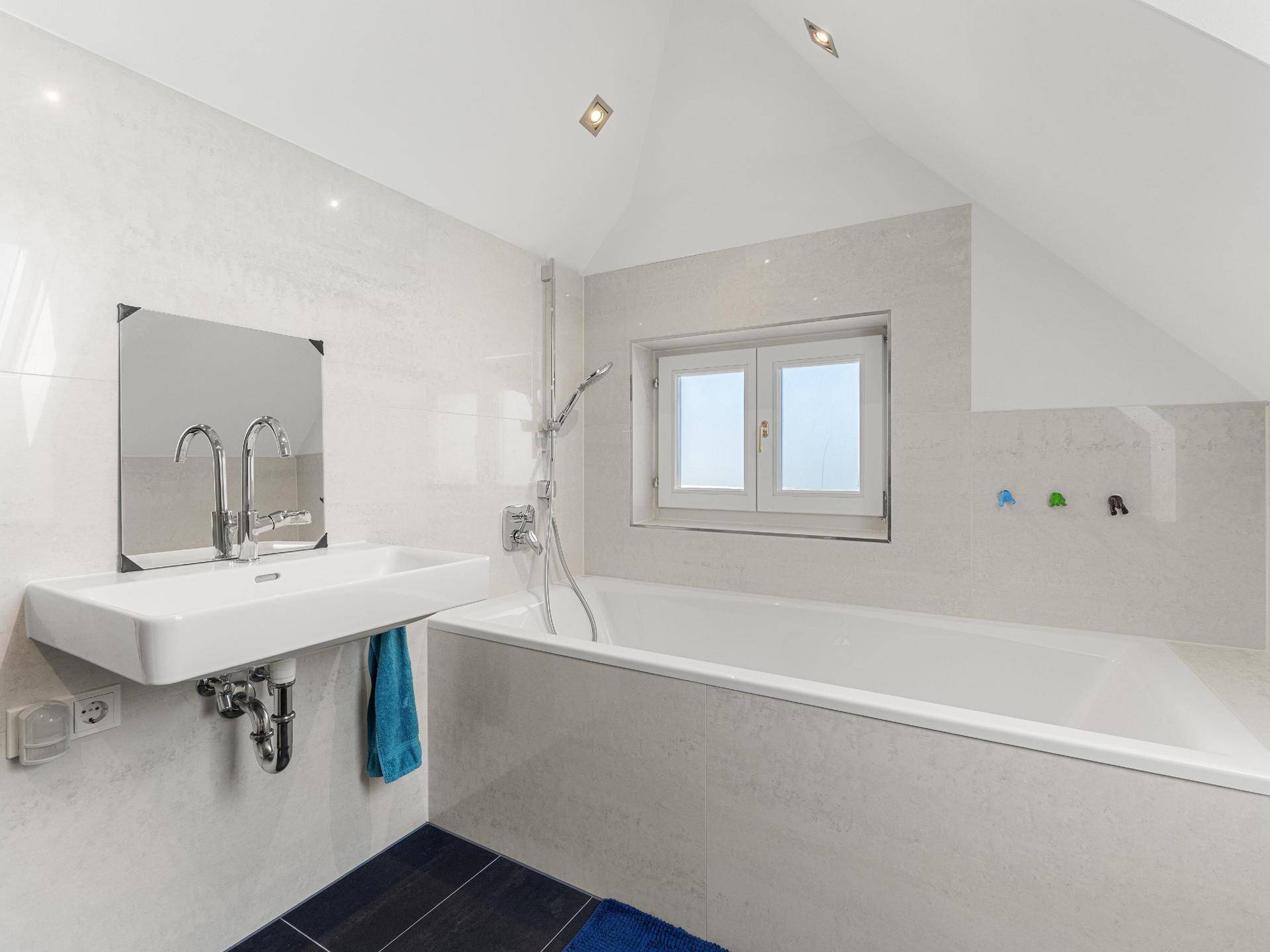 Modernes Badezimmer mit Badewanne, Einzelwaschbecken und Dachschräge, hell gefliest.