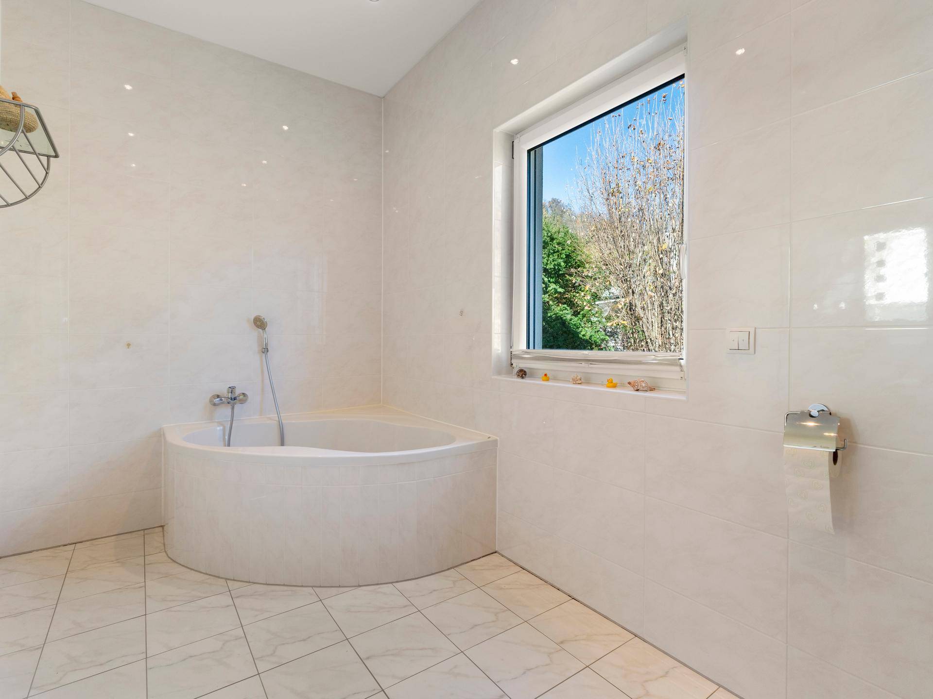 Geräumiges Badezimmer mit Eckbadewanne, Fenster und hellen Fliesen, viel Tageslicht.