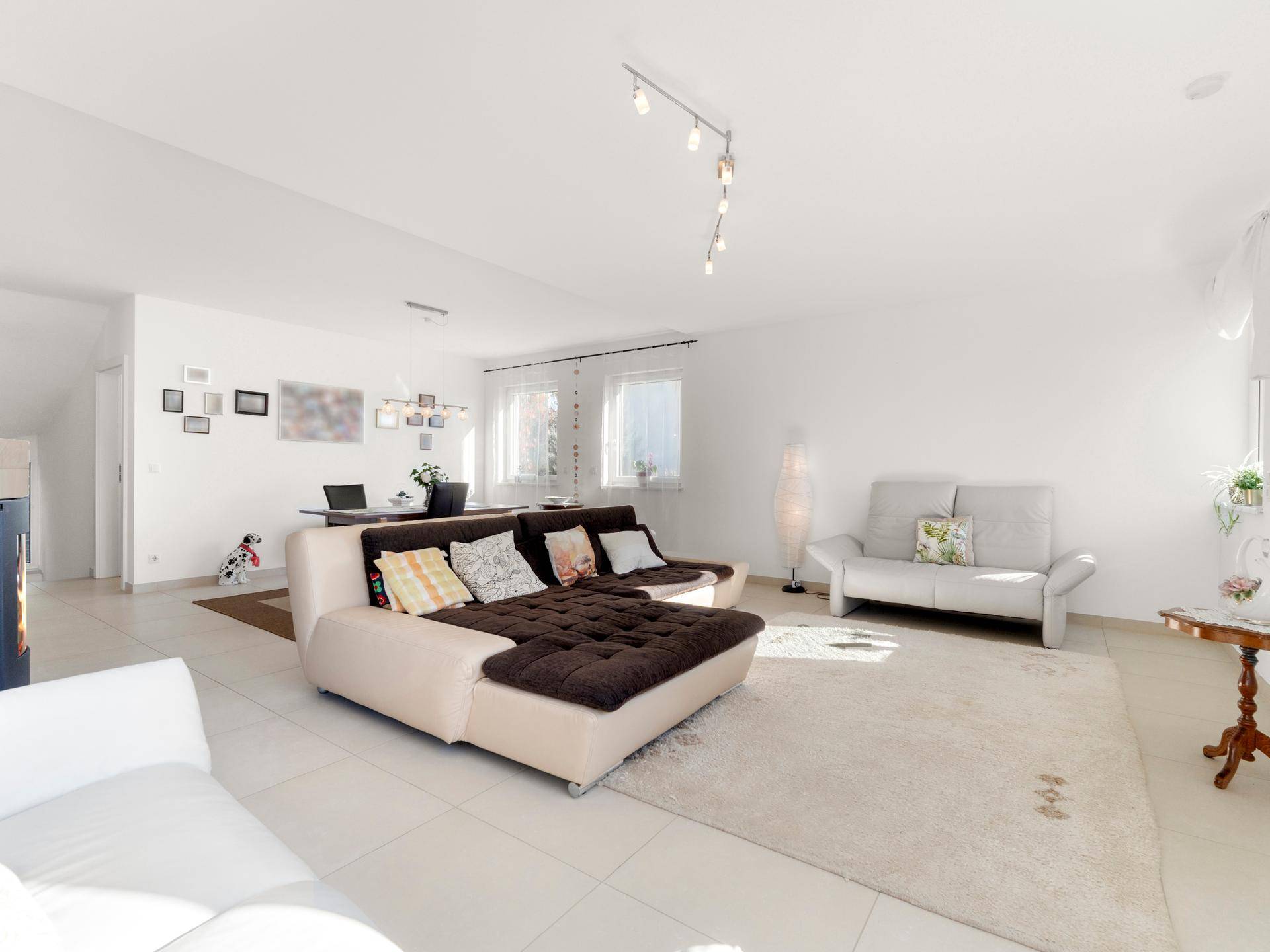Helles Wohnzimmer mit großem Sofa, Fliesenboden und viel Tageslicht, offen gestaltet.