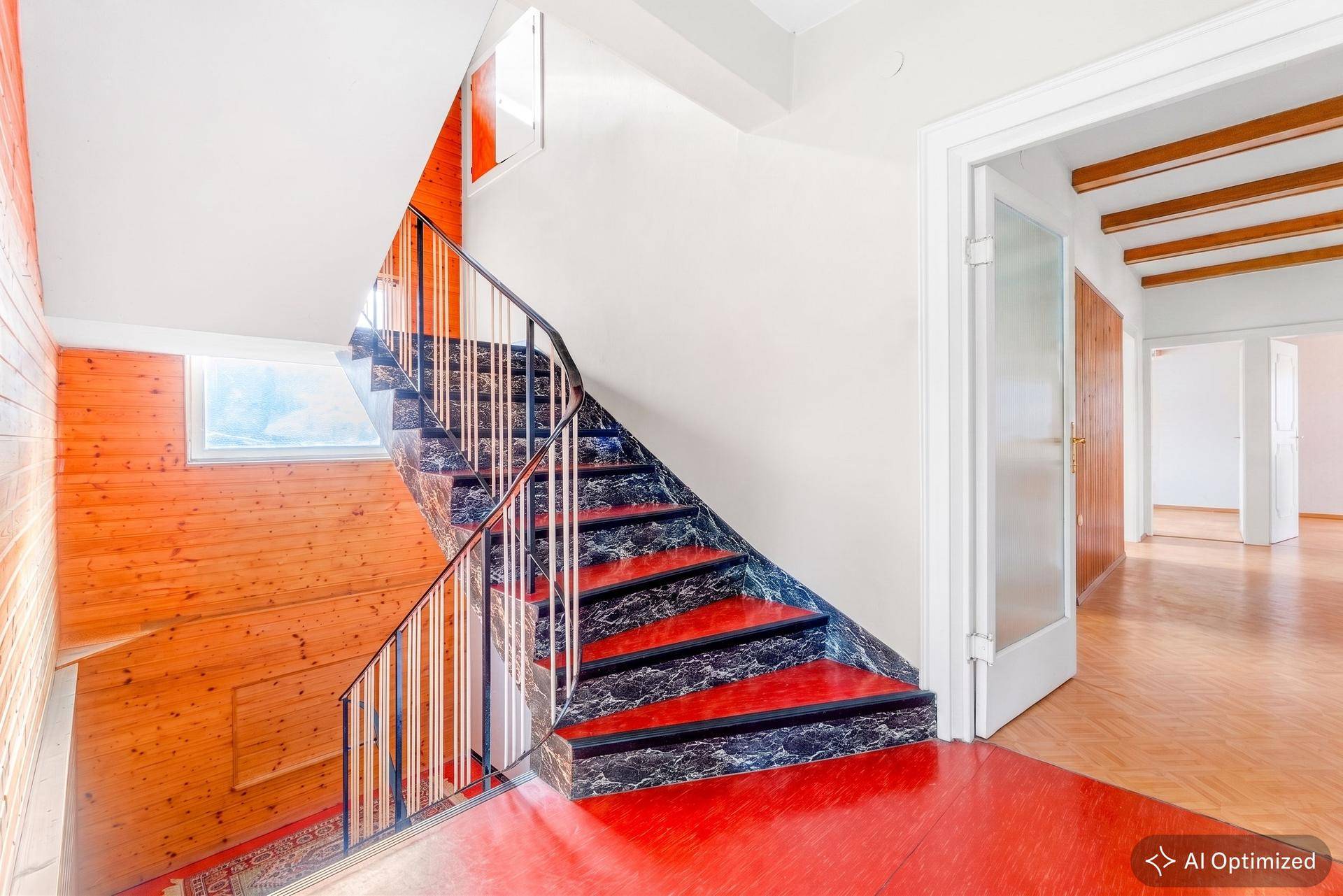 Heller Flur mit markanter Treppe, Holzvertäfelung und roten Akzenten im Eingangsbereich.