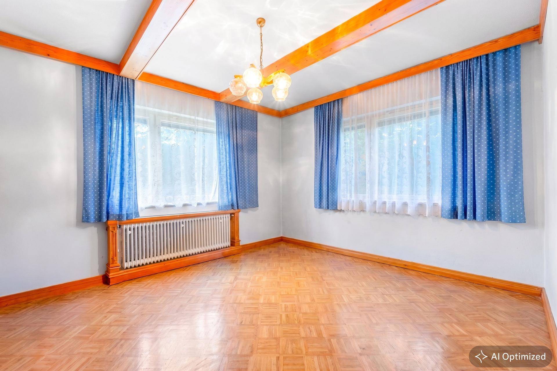 Heller Raum mit Parkettboden, weißen Wänden und sichtbaren Holzdeckenbalken, blaue Vorhänge.