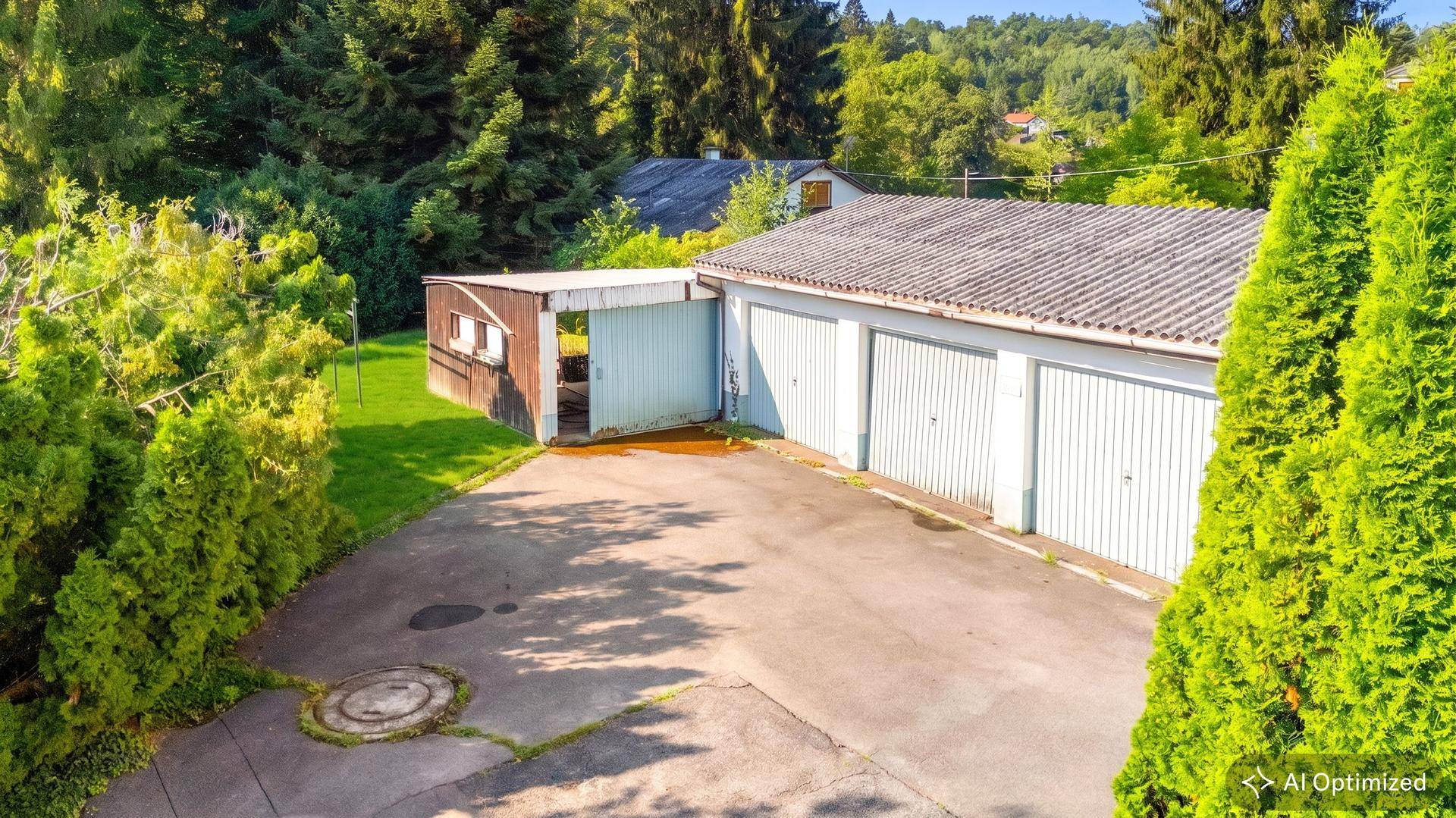 Dreifachgarage und ein kleiner Schuppen mit gepflasterter Zufahrt, umgeben von Grün.