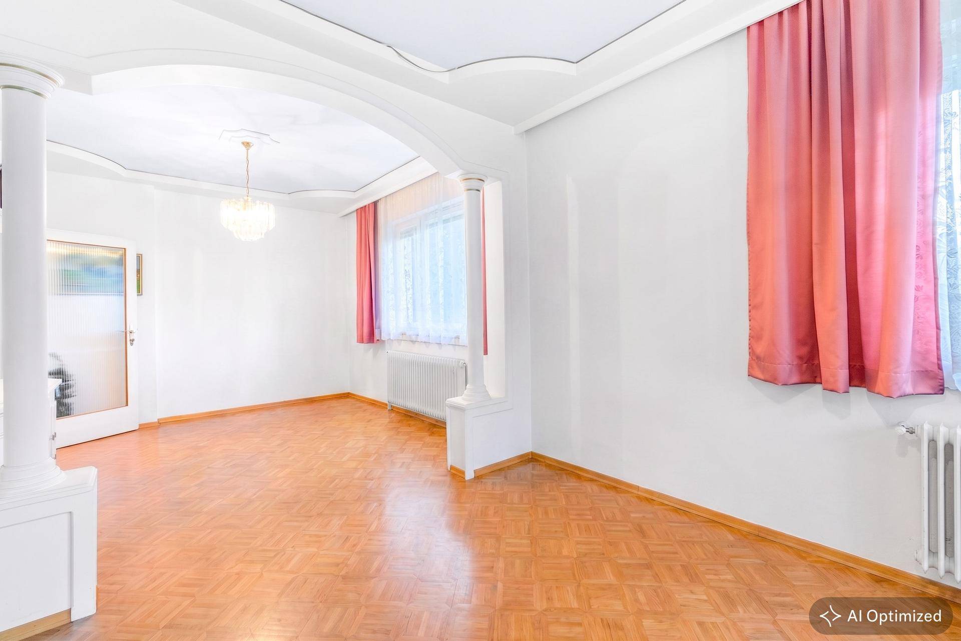 Geräumiges Wohnzimmer mit Parkettboden, weißen Wänden und dekorativer Stuckdecke.