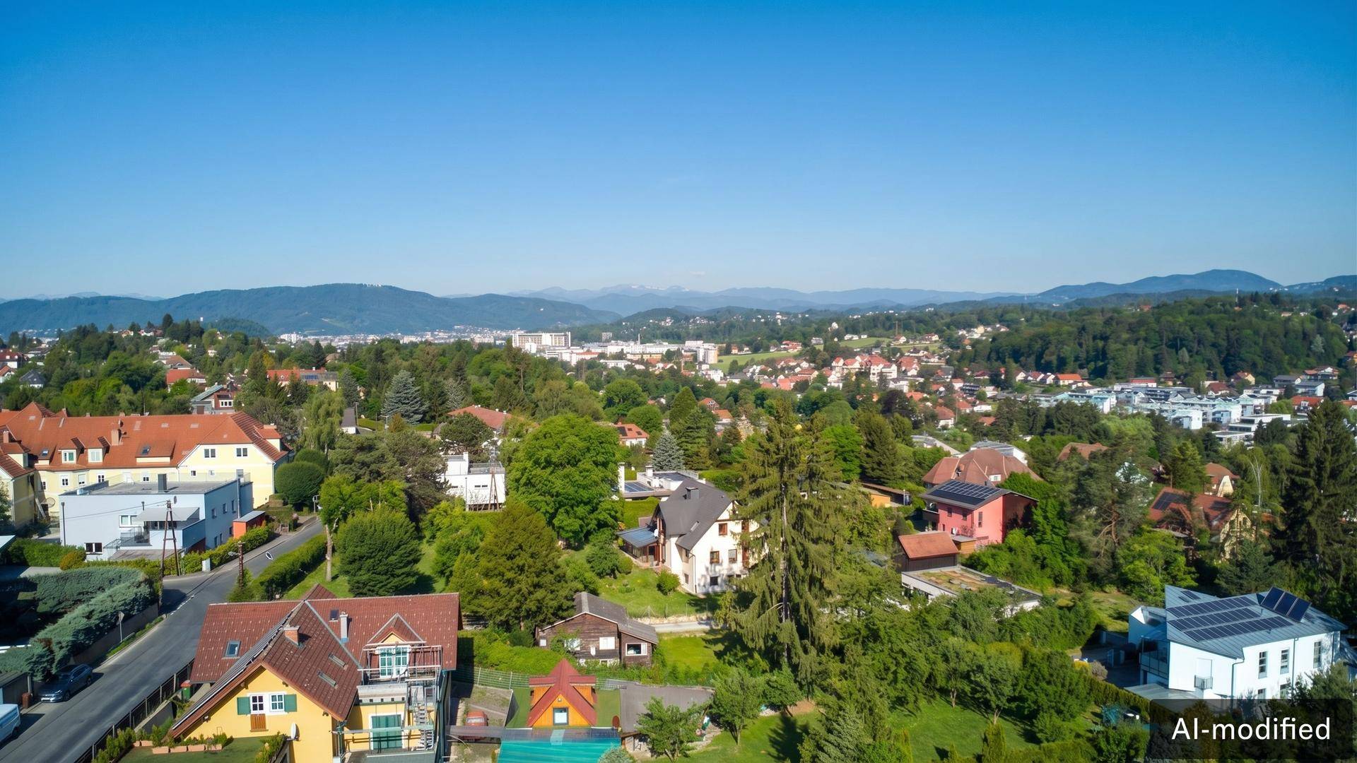 Panoramablick über eine Wohnsiedlung mit viel Grün und Bergen im Hintergrund.