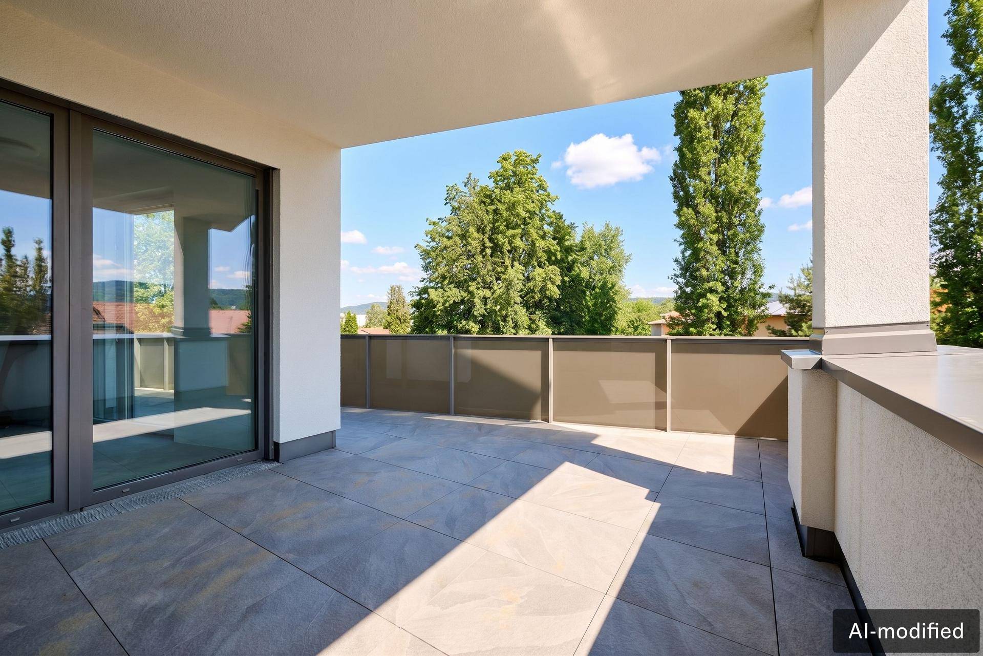Großzügige, geflieste Terrasse mit Schiebetüren und weitem Blick auf grüne Bäume.