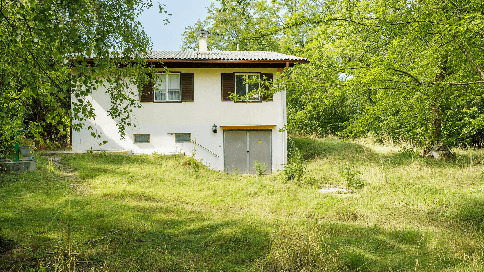 Vorderansicht eines Einfamilienhauses mit weißer Fassade, Fensterläden und Garagentor im Untergeschoss.
