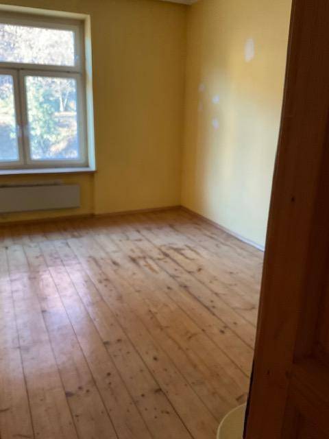 Geräumiges Zimmer mit Holzdielenboden und gelben Wänden, bereit zur Renovierung.