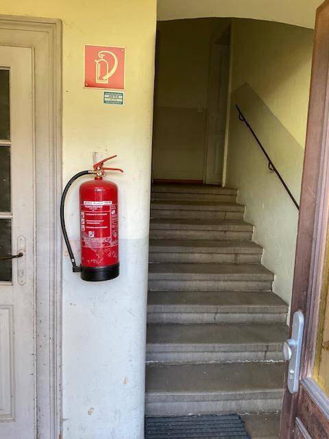 Eingangsbereich mit Steintreppe und Feuerlöscher, der zu den oberen Etagen führt.