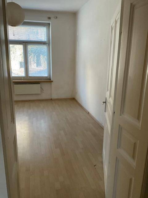 Helles Zimmer mit hellem Laminatboden und Fenster mit Jalousien.