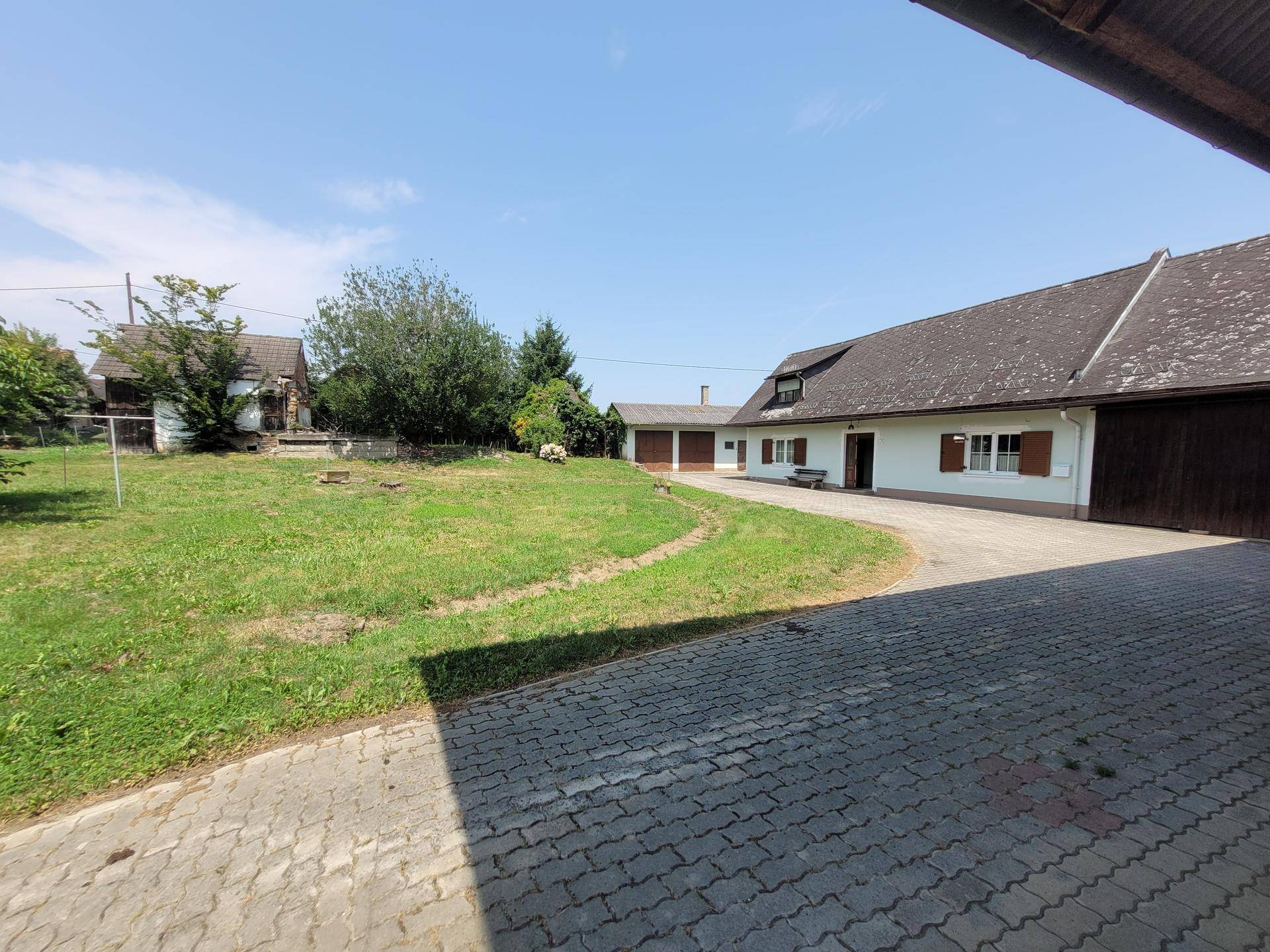 Weitläufiger Gartenbereich mit gepflasterter Zufahrt und Blick auf das ländliche Anwesen unter blauem Himmel.