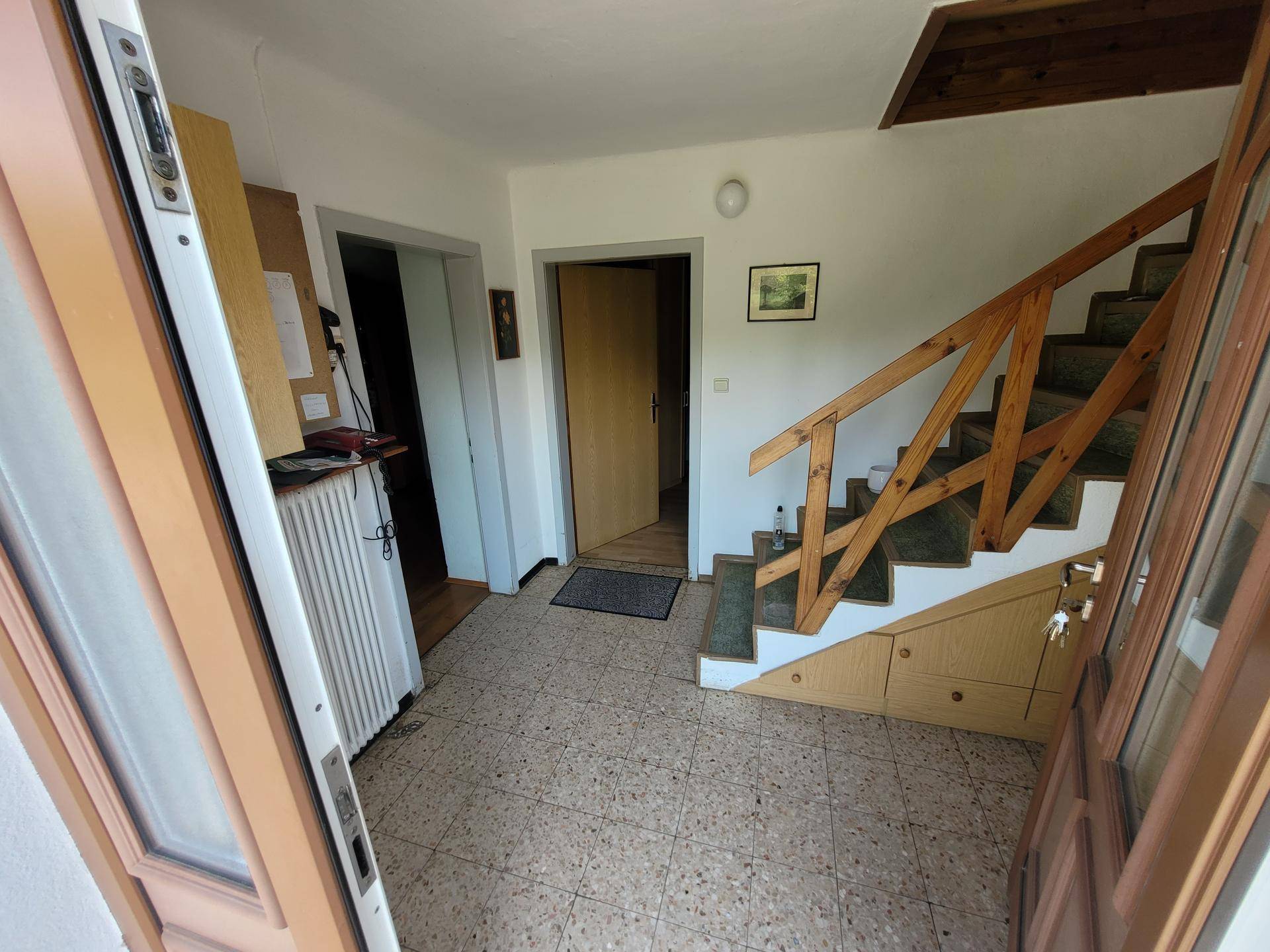 Eingangsbereich mit Treppe, Holzgeländer und Terrazzoboden, der zu den oberen Etagen führt.