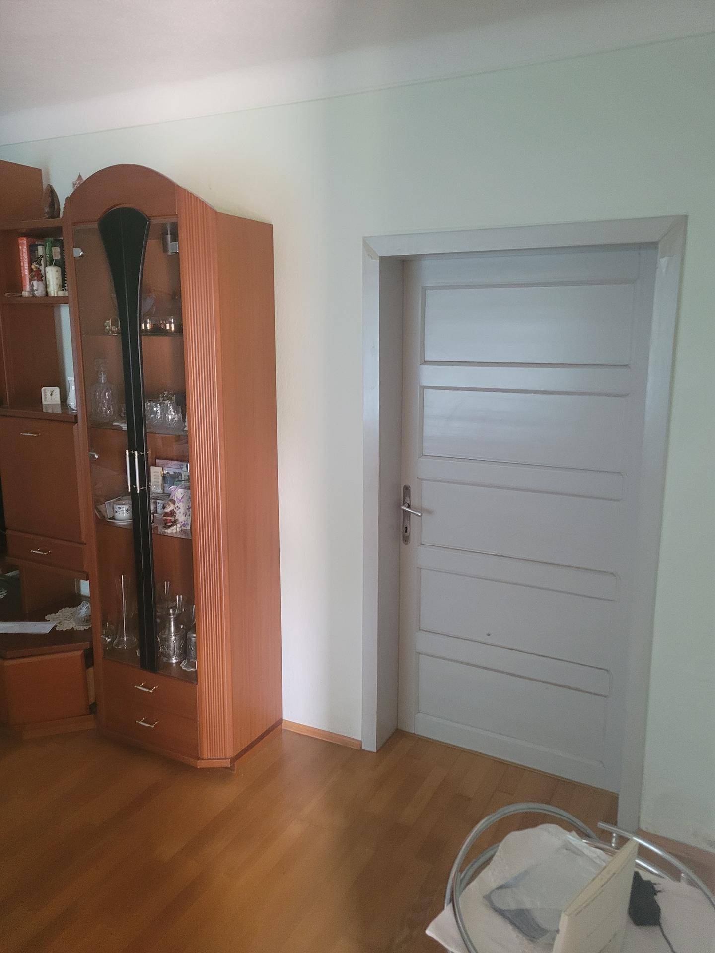 Innenraum mit hellem Laminatboden und einem Holzvitrinenschrank, der Dekorationsartikel enthält.
