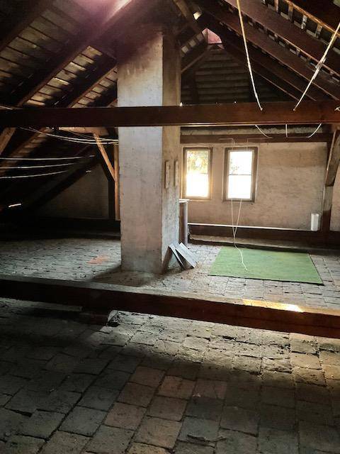 Unausgebauter Dachboden mit Holzbalken und Ziegelboden, bietet Ausbaupotenzial.