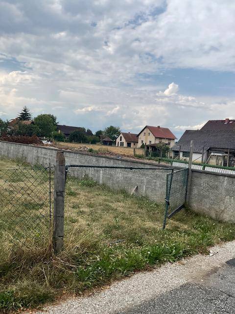 Grundstück mit Zaun und Betonmauer, umgeben von ländlicher Bebauung und Natur.