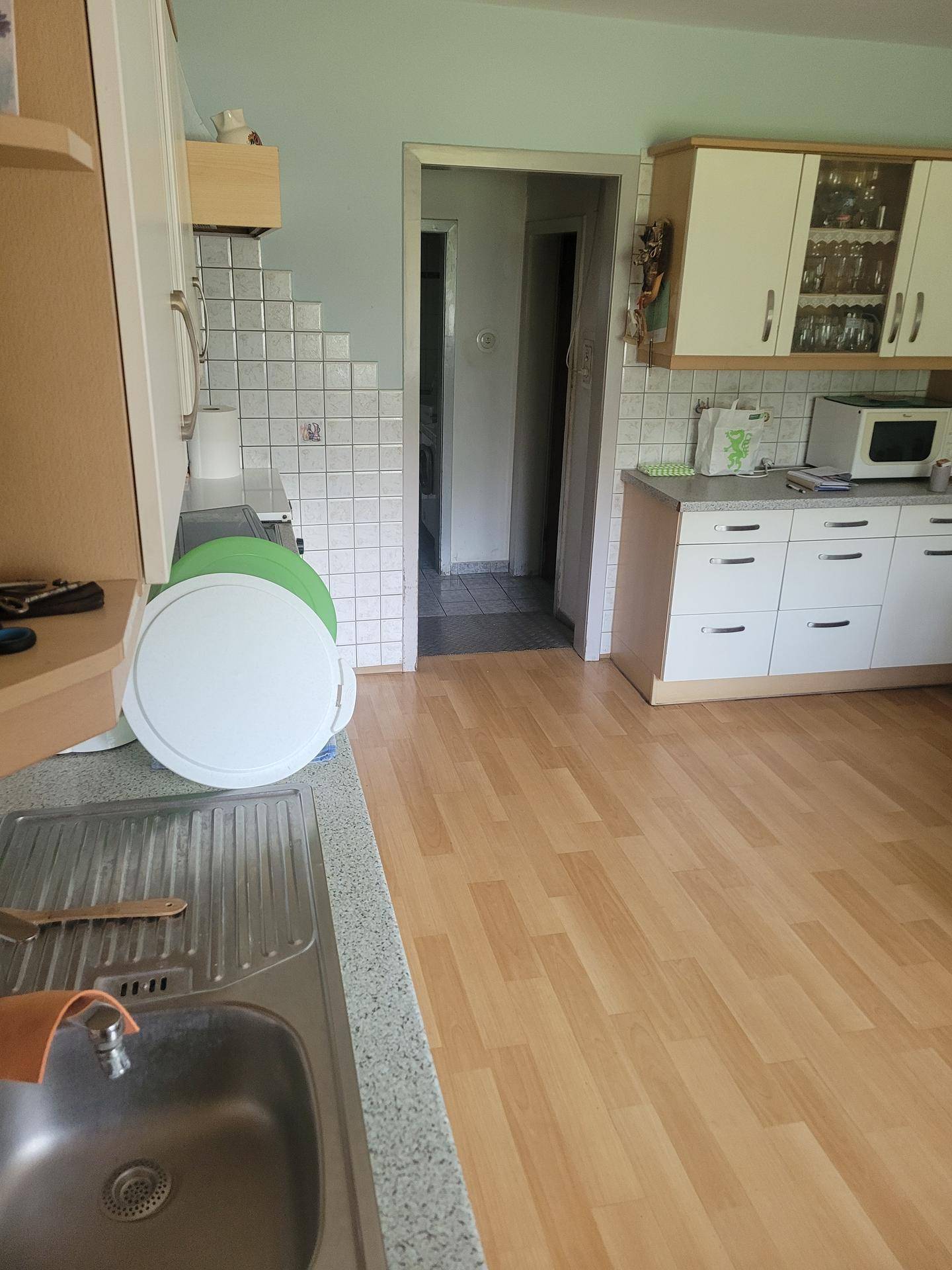 Küche mit hellem Laminatboden, weißen Hängeschränken und gefliestem Arbeitsbereich.