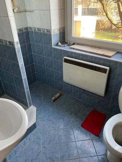 Badezimmer mit blauen Fliesen, Dusche und Fenster, das Tageslicht spendet.