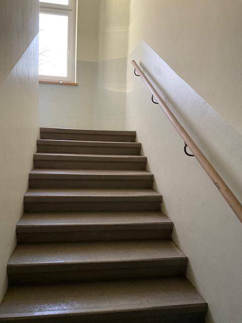Helles Treppenhaus mit Holzgeländer und Fenster, das natürliches Licht hereinlässt.