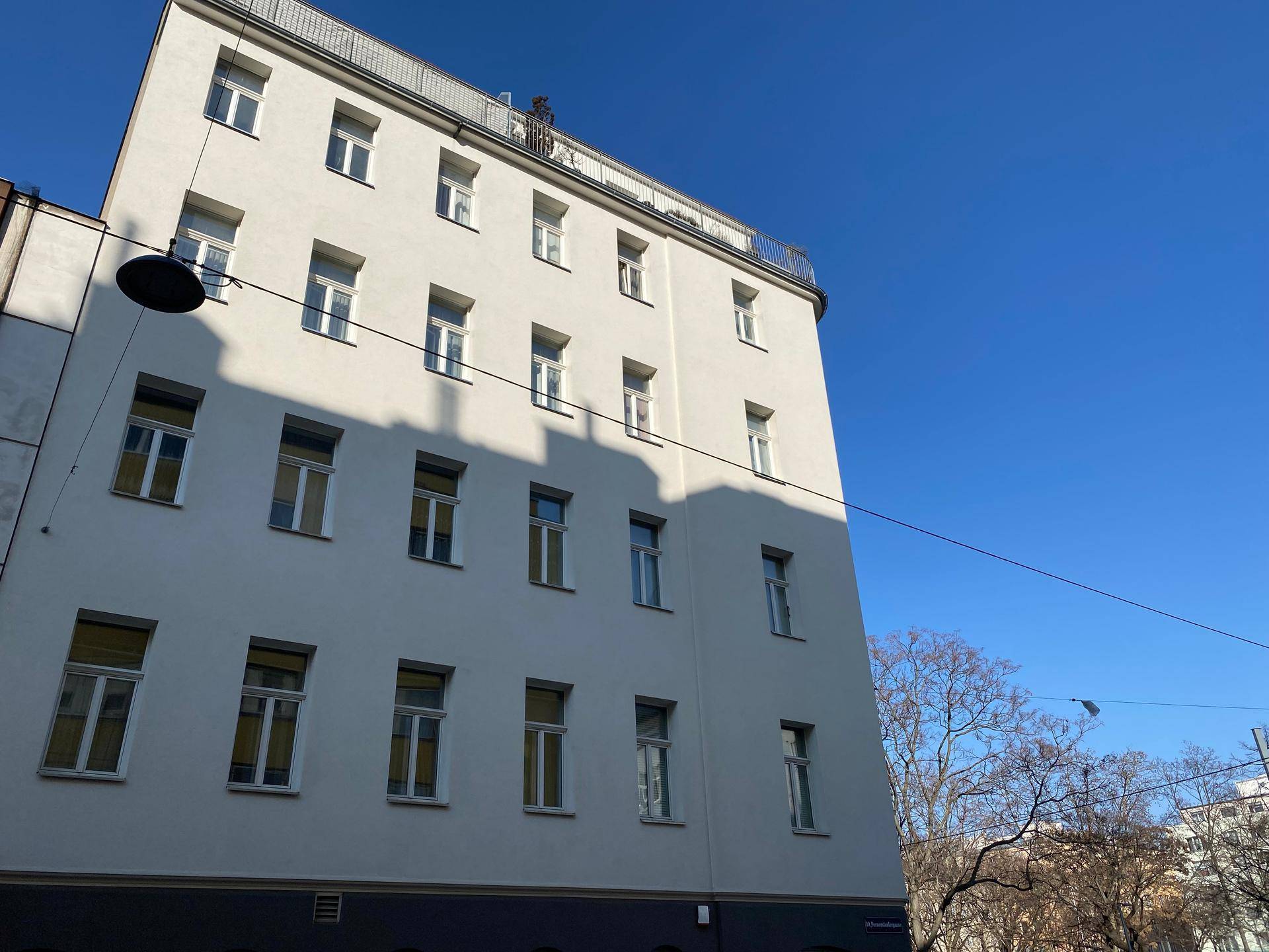 Weiße Fassade eines Mehrfamilienhauses mit vielen Fenstern unter blauem Himmel.
