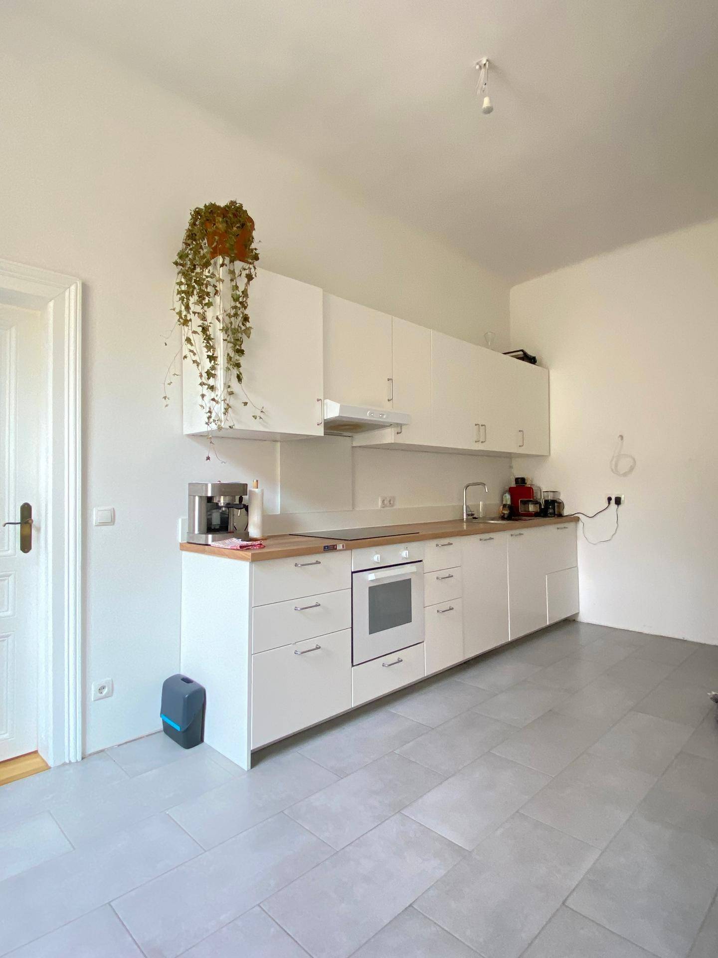 Moderne weiße Küche mit Holz-Arbeitsplatte, Fliesenboden und Hängeschränken.